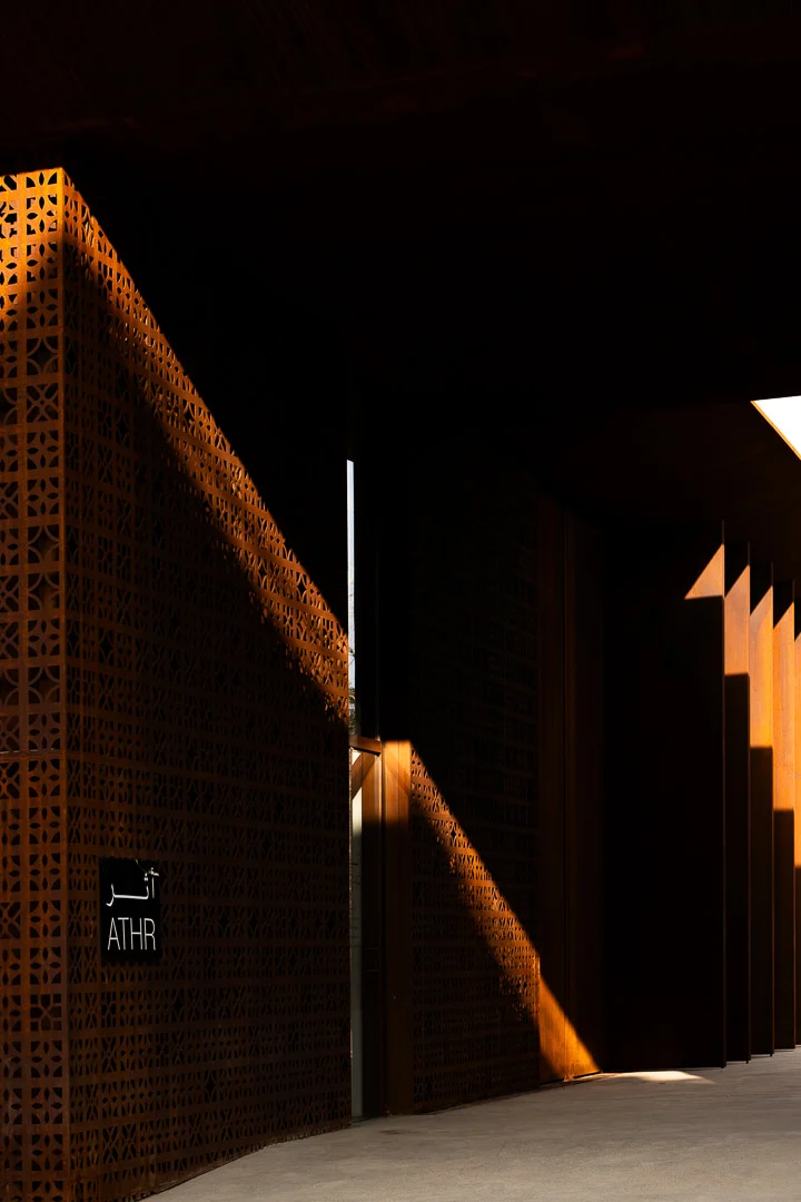 Angolo in ombra dello schermo forato con un'insegna ATHR in arabo e inglese, attraversato da luce obliqua – Design Space AlUla, Arabia Saudita, 2024 – architettura