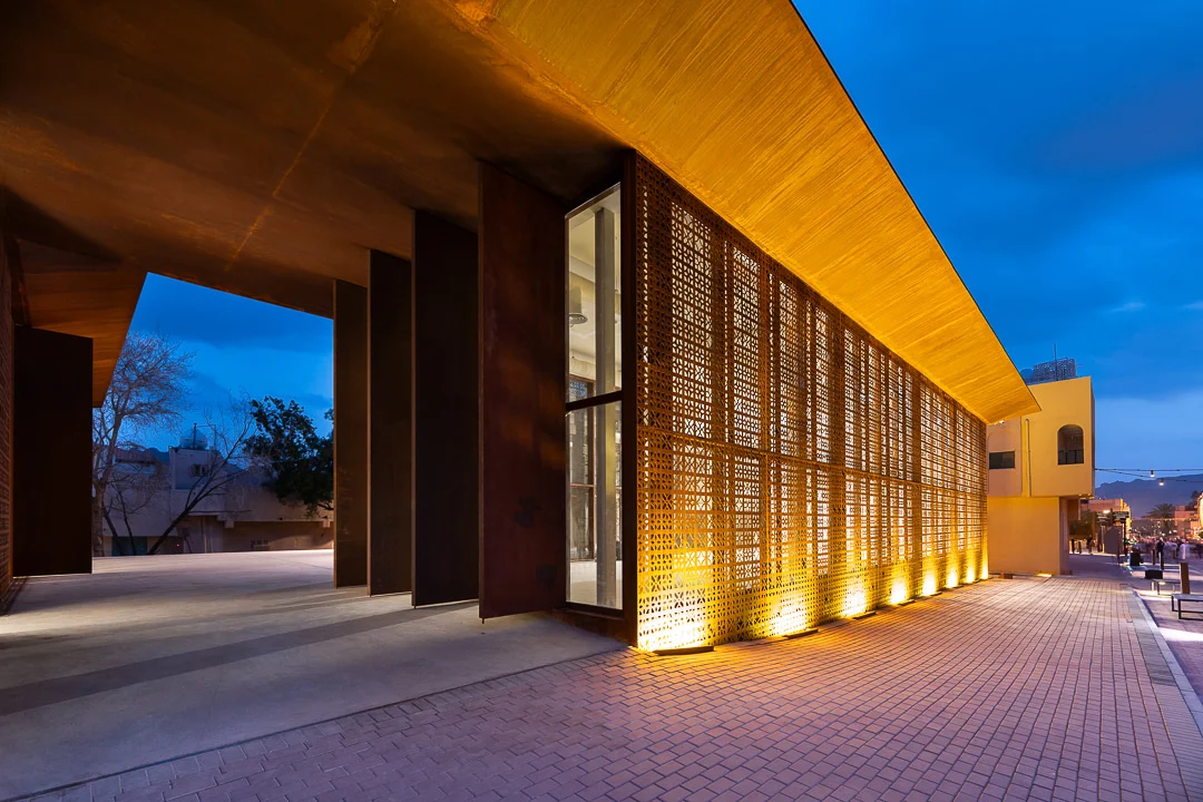 Vista laterale al tramonto dello schermo forato illuminato e del profondo sbalzo del tetto sopra un passaggio coperto – Design Space AlUla, Arabia Saudita, 2024 – architettura