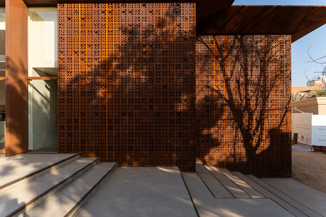 Ombre di alberi sullo schermo in metallo forato color ruggine sopra ampi gradini in cemento – Design Space AlUla, Arabia Saudita, 2024 – architettura