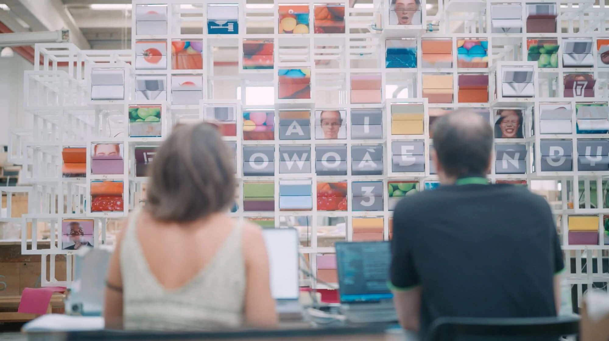 Due persone ai portatili davanti a La Nuvola durante i test, i moduli mostrano lettere, volti e colori – La Nuvola al Cirfood District, Reggio Emilia, Italia, 2022 – progettazione di installazioni cinetiche