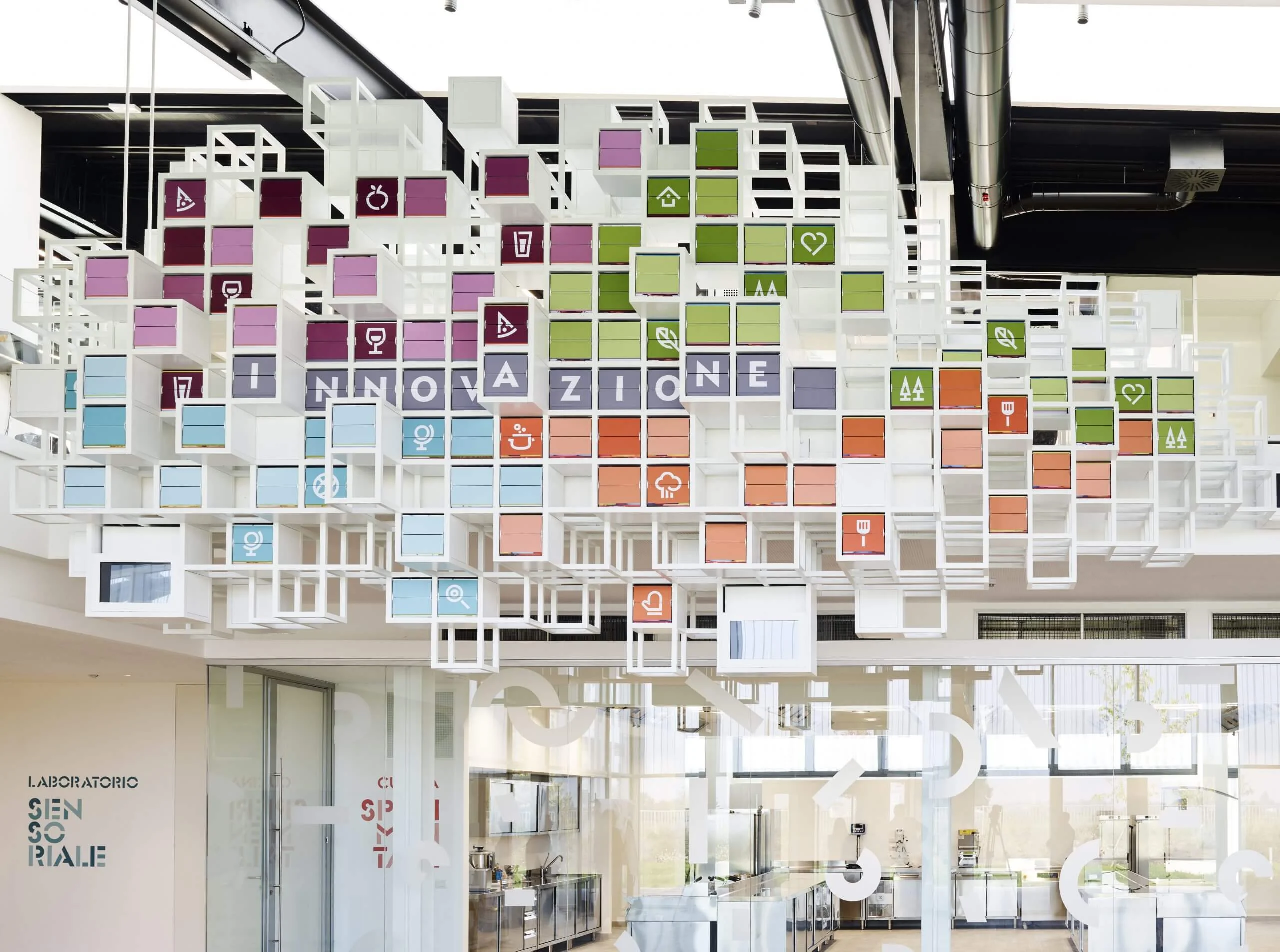 La Nuvola vista dal basso: cubi a telaio bianco con icone colorate di cibo e la parola "Innovazione" – La Nuvola al Cirfood District, Reggio Emilia, Italia, 2022 – progettazione di installazioni cinetiche