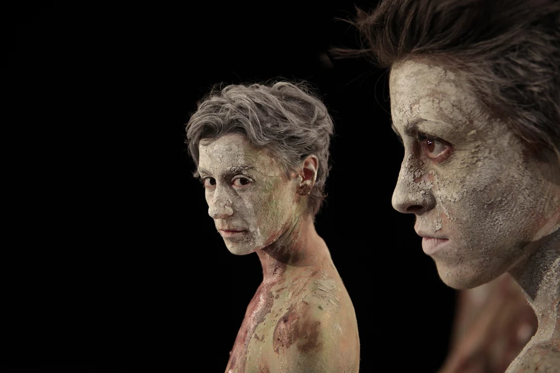 Dettaglio di due artisti con il corpo dipinto d'argilla screpolata, uno di profilo, su sfondo nero – I Shardana al Teatro Lirico di Cagliari, Italia, 2013 – scenografia d'opera