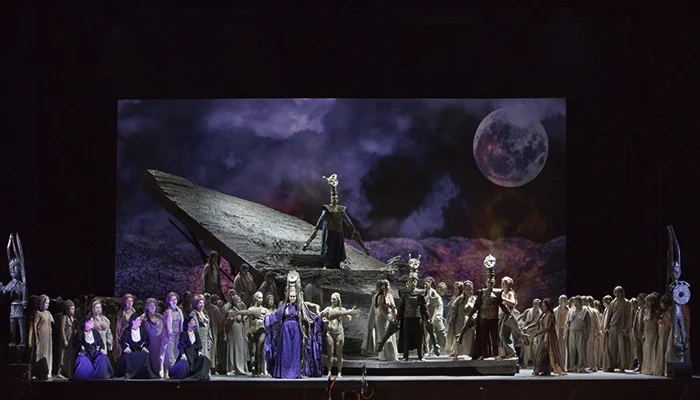 I Shardana al Teatro Lirico: coro davanti a una lastra di pietra inclinata sotto una luna proiettata – I Shardana al Teatro Lirico di Cagliari, Italia, 2013 – scenografia d'opera