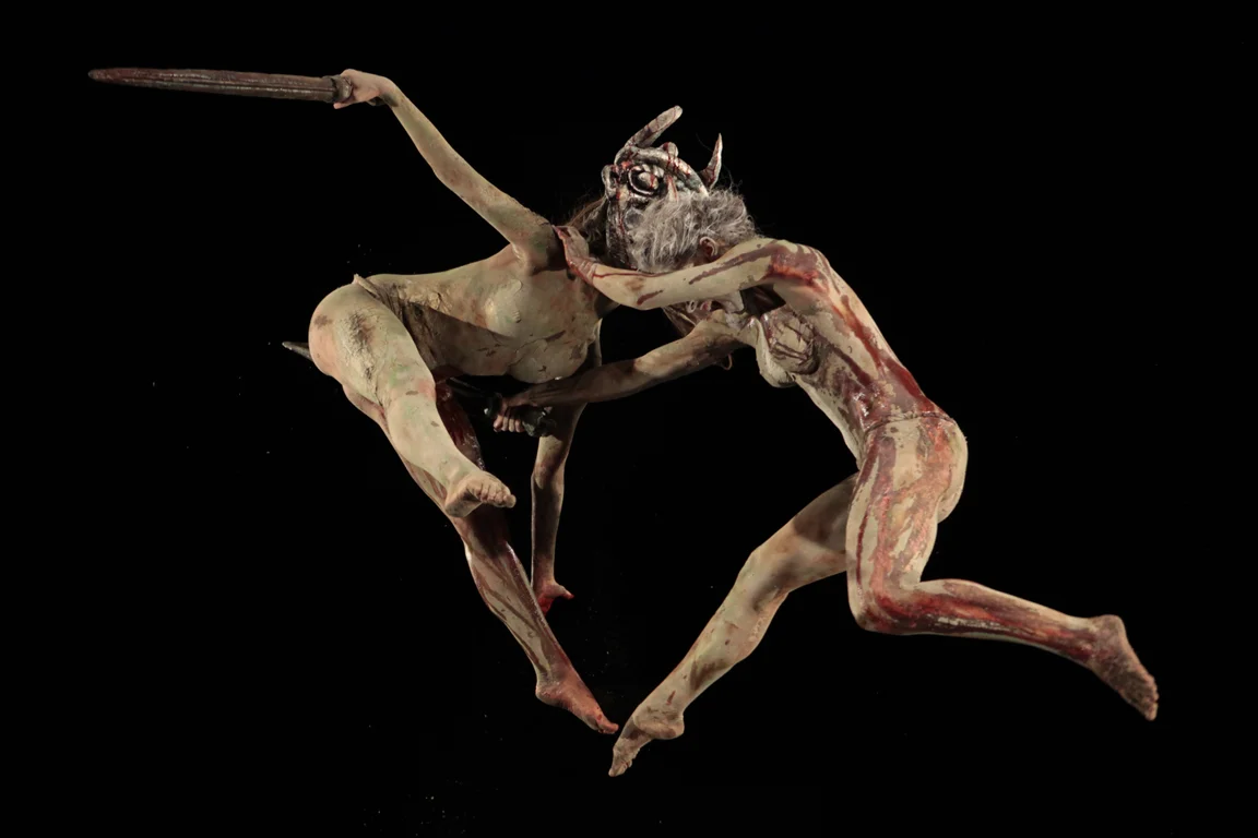 Due danzatori coperti d'argilla saltano e combattono in aria con le spade su sfondo nero – I Shardana al Teatro Lirico di Cagliari, Italia, 2013 – scenografia d'opera