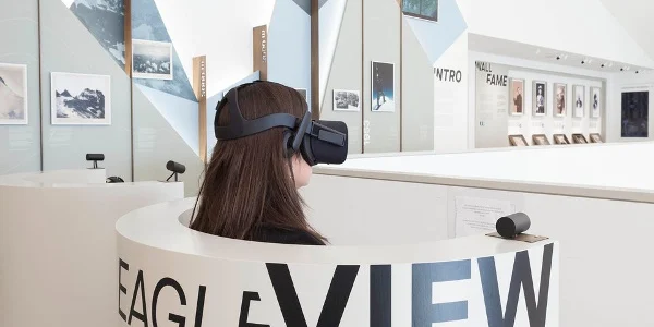 Visitatore con un visore VR nella postazione curva Eagle View, con foto esposte sulle pareti alle spalle – Lumen Museo della fotografia di montagna, Plan de Corones, Italia, 2018 – architettura