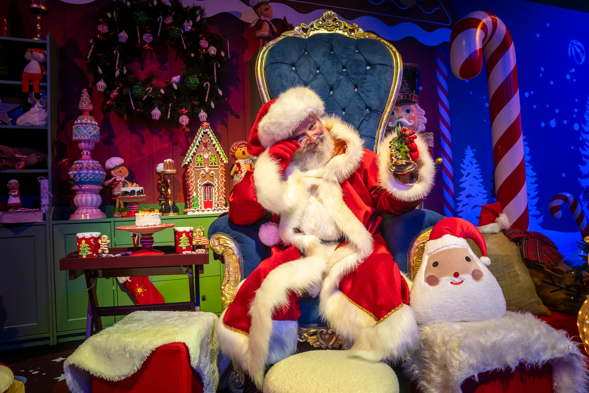 Babbo Natale su un trono di velluto blu in una scenografia accogliente con bastoncini di zucchero, giocattoli e una casetta di pan di zenzero – A Christmas Magic all'Allianz MiCo, Milano, Italia, 2023 – progettazione di eventi