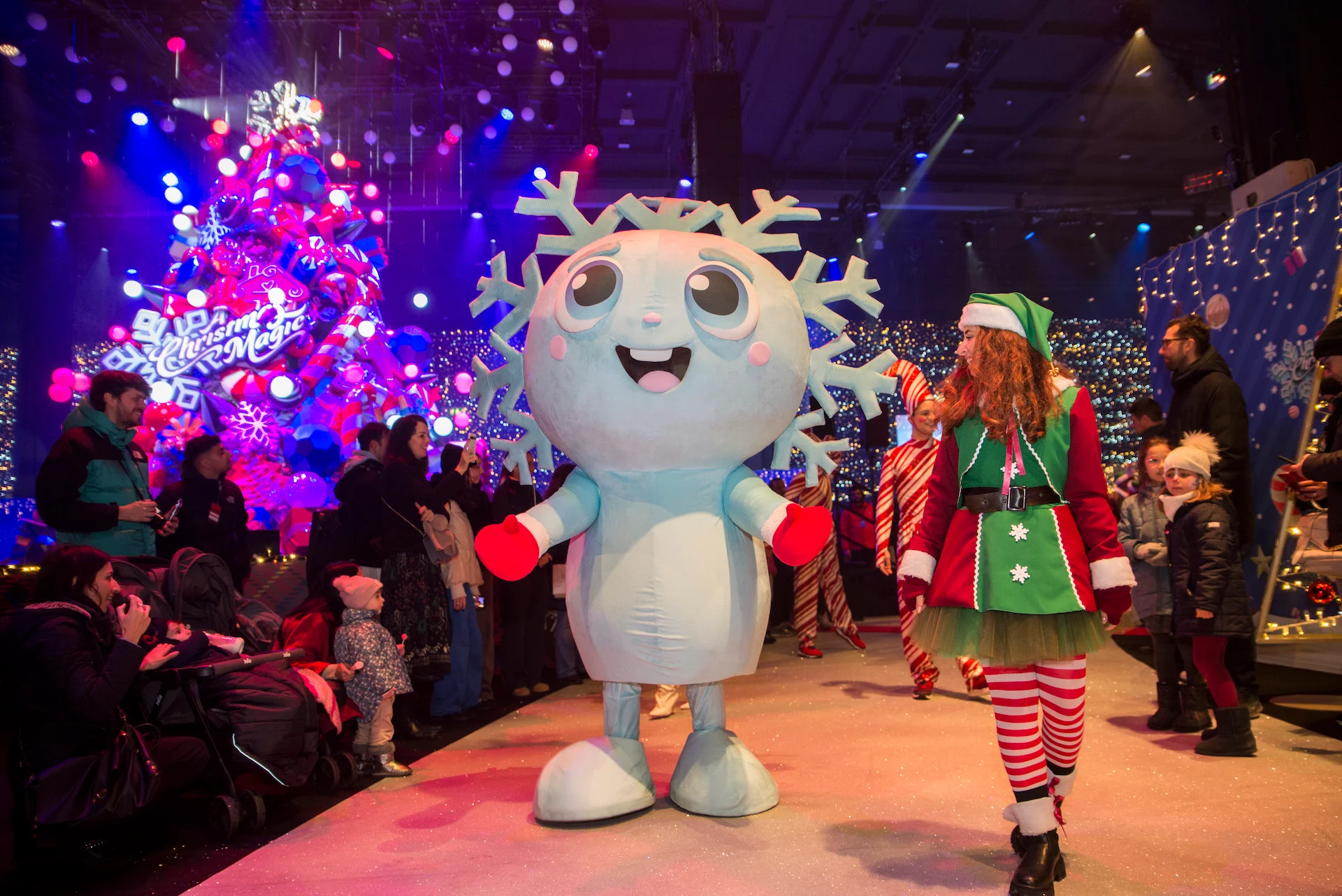 Mascotte a forma di fiocco di neve ed elfo che sfilano tra le famiglie davanti all'albero di Natale illuminato – A Christmas Magic all'Allianz MiCo, Milano, Italia, 2023 – progettazione di eventi