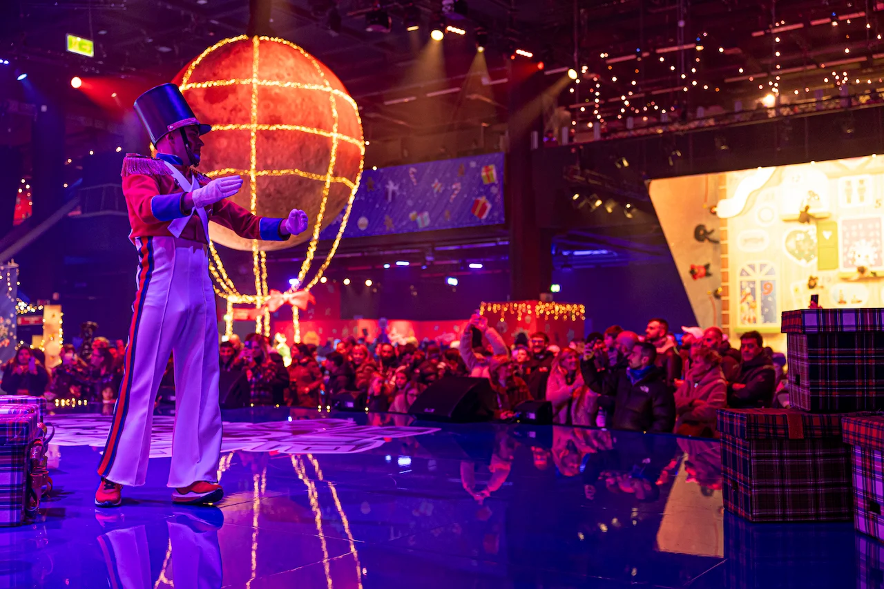 Artista con cilindro e costume da soldatino su un palco riflettente, una mongolfiera luminosa dietro – A Christmas Magic all'Allianz MiCo, Milano, Italia, 2023 – progettazione di eventi