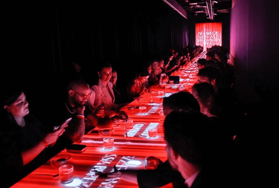 Ospiti a un lungo tavolo LED acceso di rosso, con testi proiettati e drink – Campari Discover Red Party al Festival di Cannes, Francia, 2023 – progettazione di eventi
