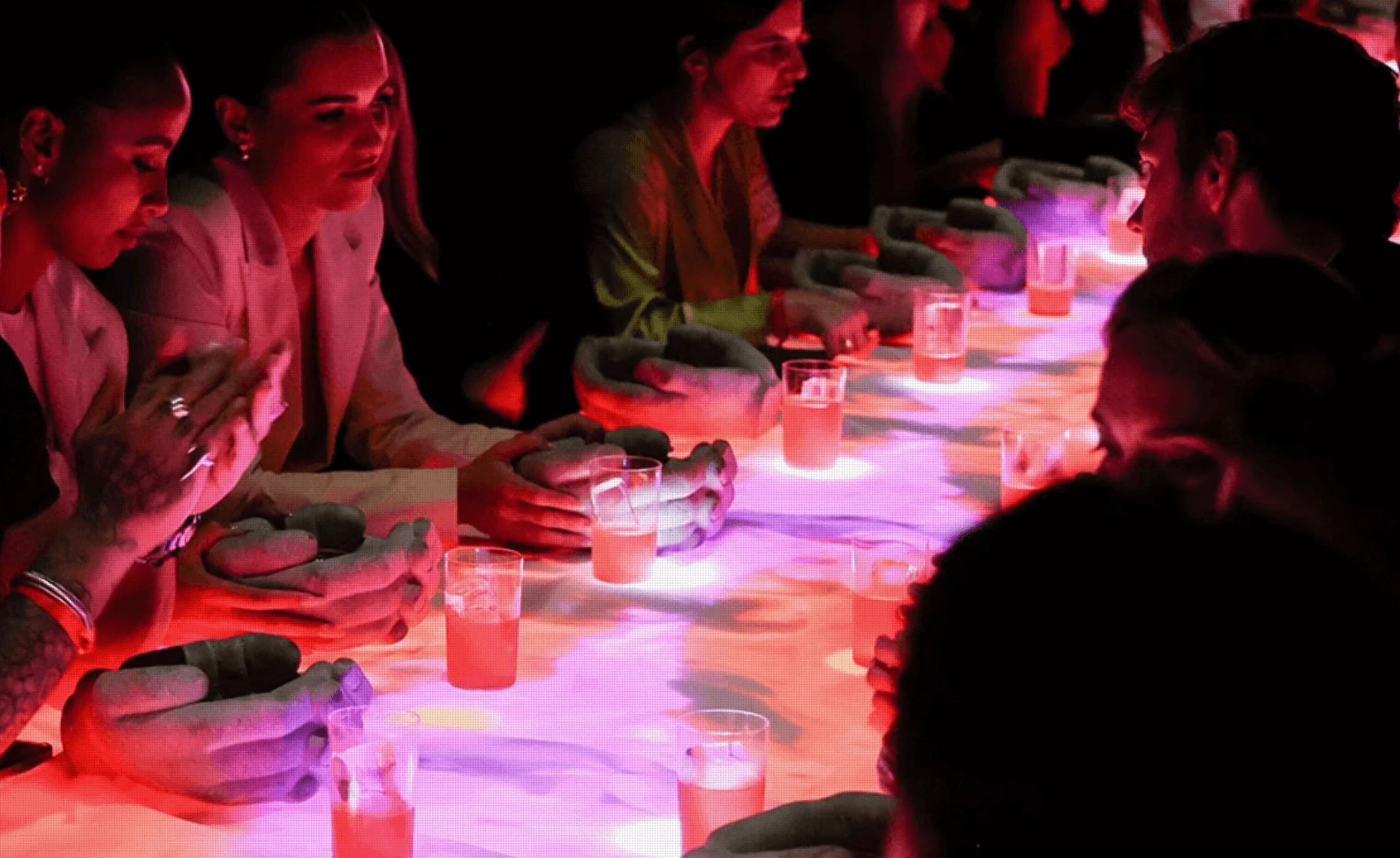 Dettaglio degli ospiti al tavolo LED, mani appoggiate accanto a proiezioni luminose e drink rosa – Campari Discover Red Party al Festival di Cannes, Francia, 2023 – progettazione di eventi