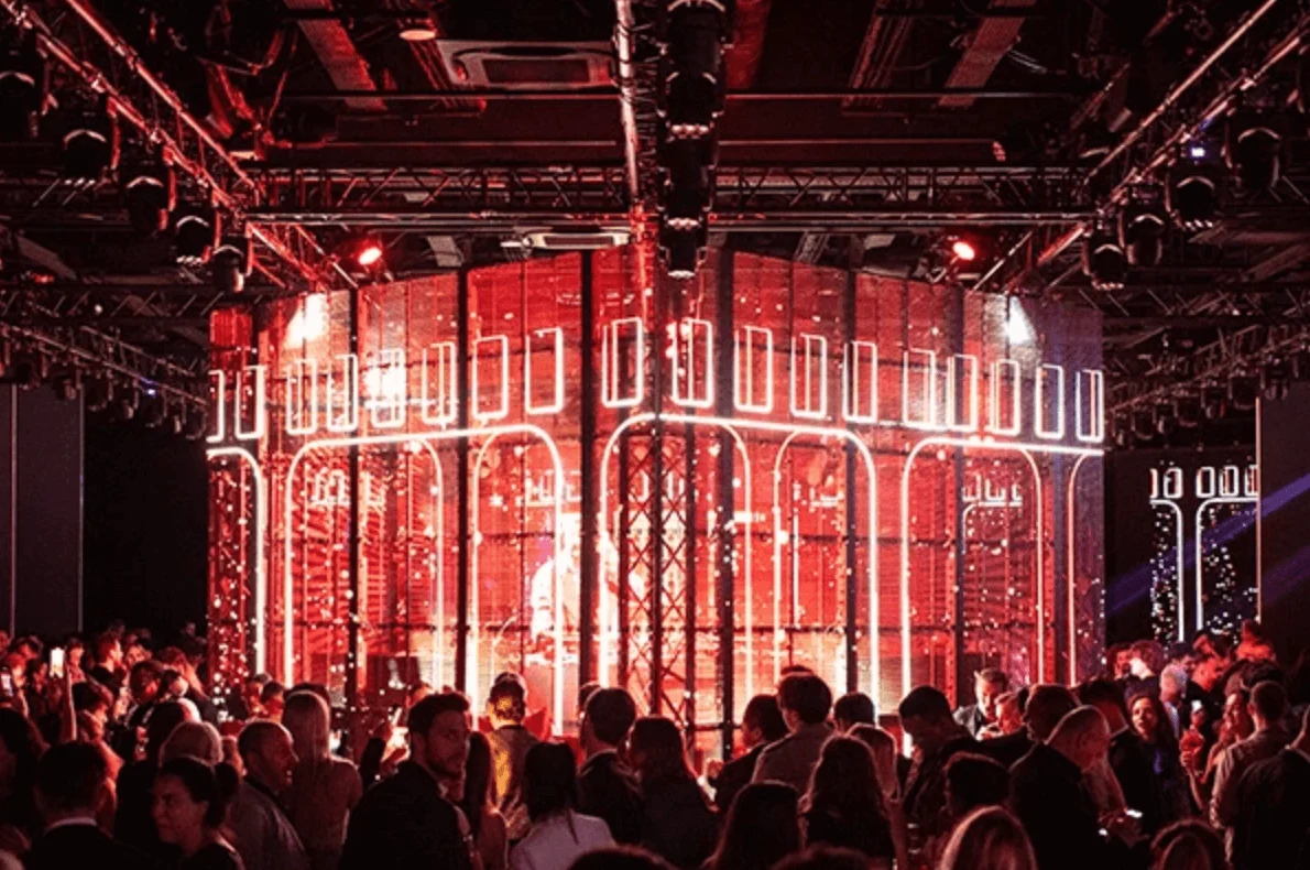 Folla intorno a una struttura cilindrica LED rossa con motivi ad arco bianchi sotto le americane delle luci – Campari Discover Red Party al Festival di Cannes, Francia, 2023 – progettazione di eventi