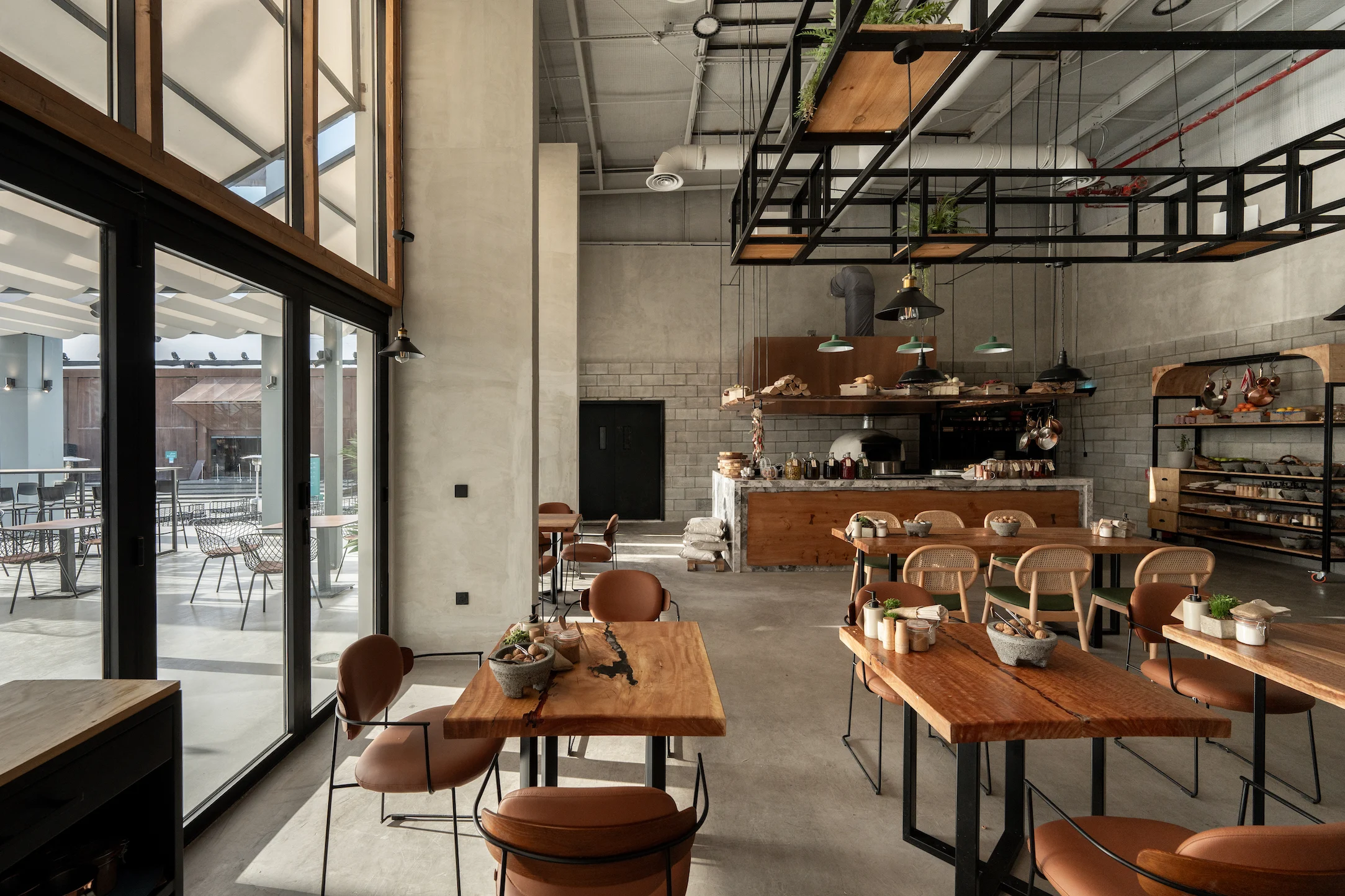 Interno del bar con tavoli in legno, sedie in pelle color cuoio, pareti in blocchi di cemento e una struttura in acciaio nero sopra – Biennale d'Arte Contemporanea di Diriyah, Riyadh, Arabia Saudita, 2024 – architettura