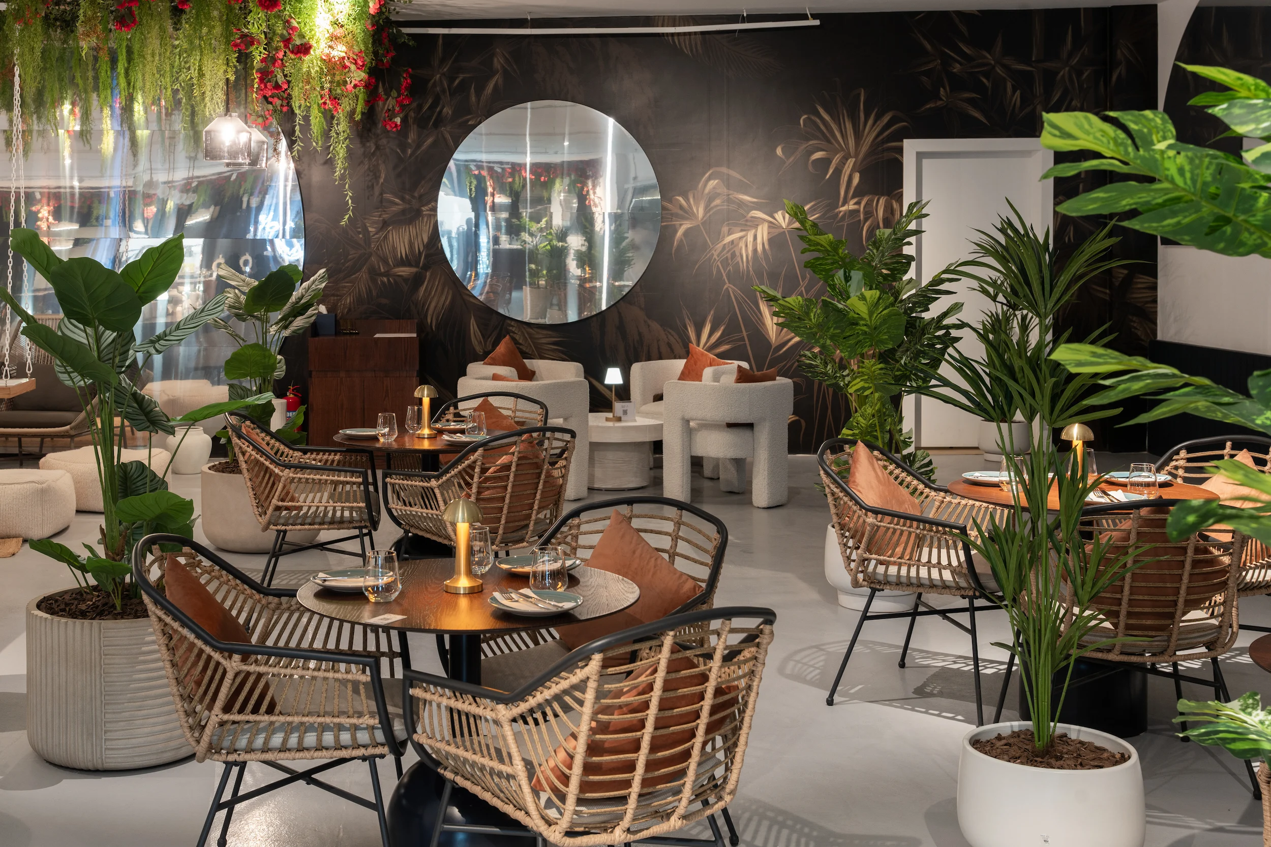 Ristorante con sedie in rattan, palme in vaso, uno specchio rotondo e carta da parati scura a foglie di palma – Biennale d'Arte Contemporanea di Diriyah, Riyadh, Arabia Saudita, 2024 – architettura
