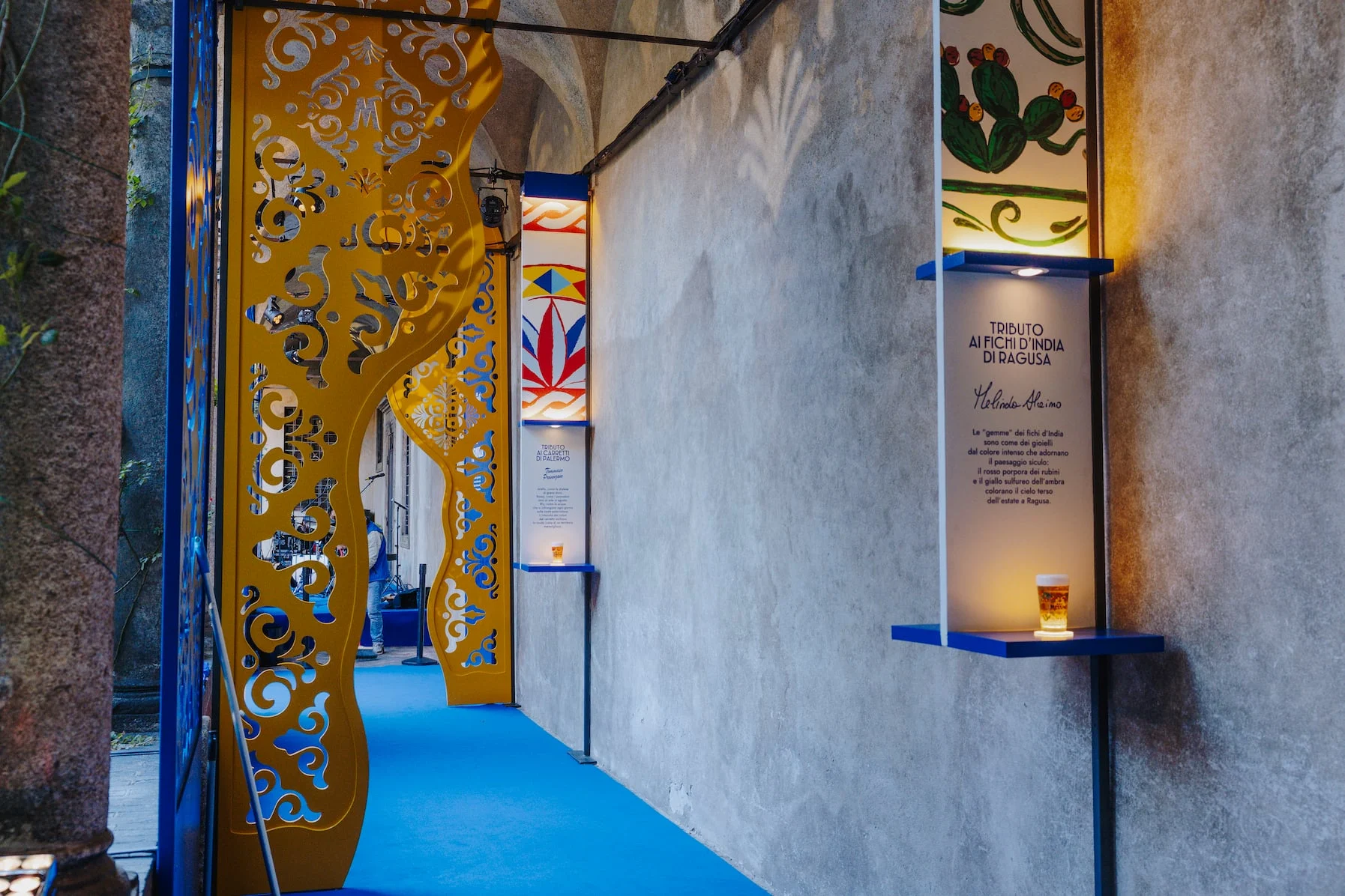 Porticato con pannelli traforati dorati, moquette blu e pannelli illustrati con un bicchiere di birra – Birra Messina Bar Meraviglia al Fuorisalone, Milano, Italia, 2024 – progettazione di eventi