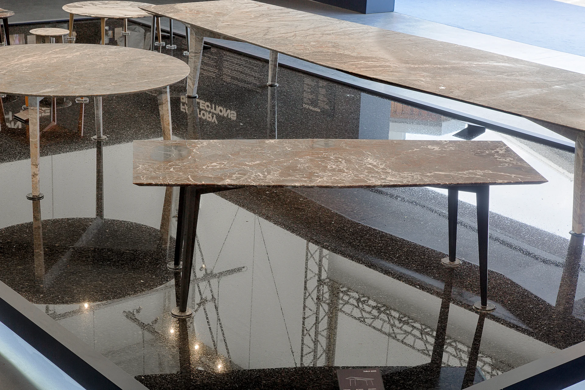 Dettaglio di tavoli in marmo con gambe sottili nell'acqua scura che riflette la copertura della fabbrica – Factory Reflections presso Sice Previt, Segrate, Italia, 2024 – allestimento espositivo