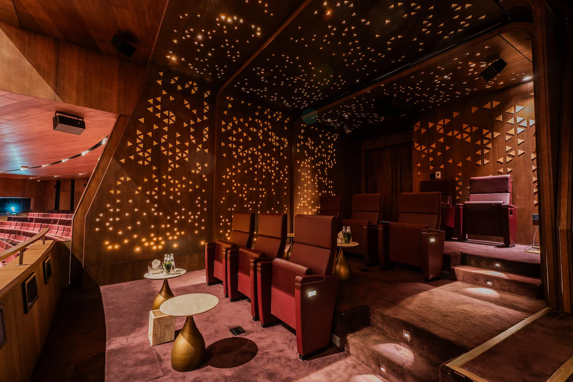 Palco privato del teatro con poltrone rosse, tavolini in ottone e pareti in legno forate da triangoli luminosi – King Fahad Cultural Center, Riyadh, Arabia Saudita, 2024 – riqualificazione architettonica