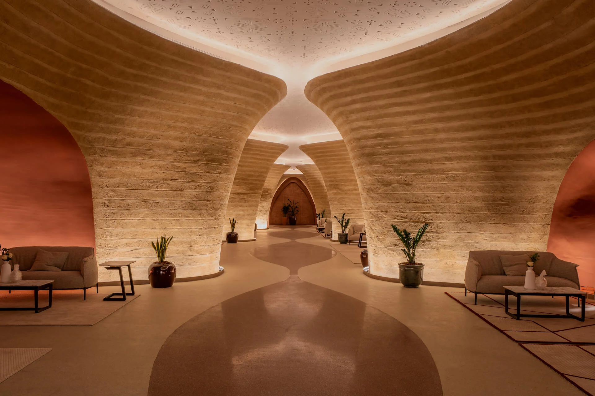 Foyer con pareti curve in terra cruda, divani lounge, piante in vaso e un soffitto ovale dalla luce soffusa – King Fahad Cultural Center, Riyadh, Arabia Saudita, 2024 – riqualificazione architettonica