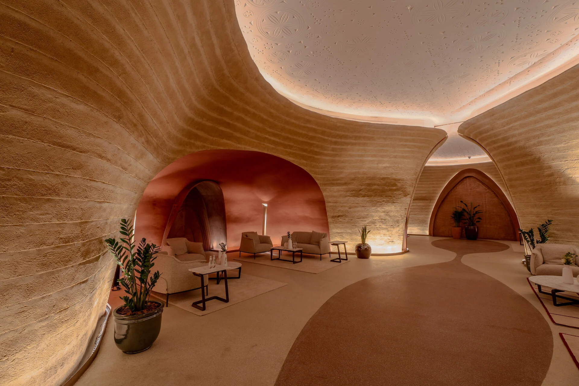 Angolo lounge in una sala curva in terra, con poltrone sotto una volta in terracotta e un motivo sinuoso sul pavimento – King Fahad Cultural Center, Riyadh, Arabia Saudita, 2024 – riqualificazione architettonica