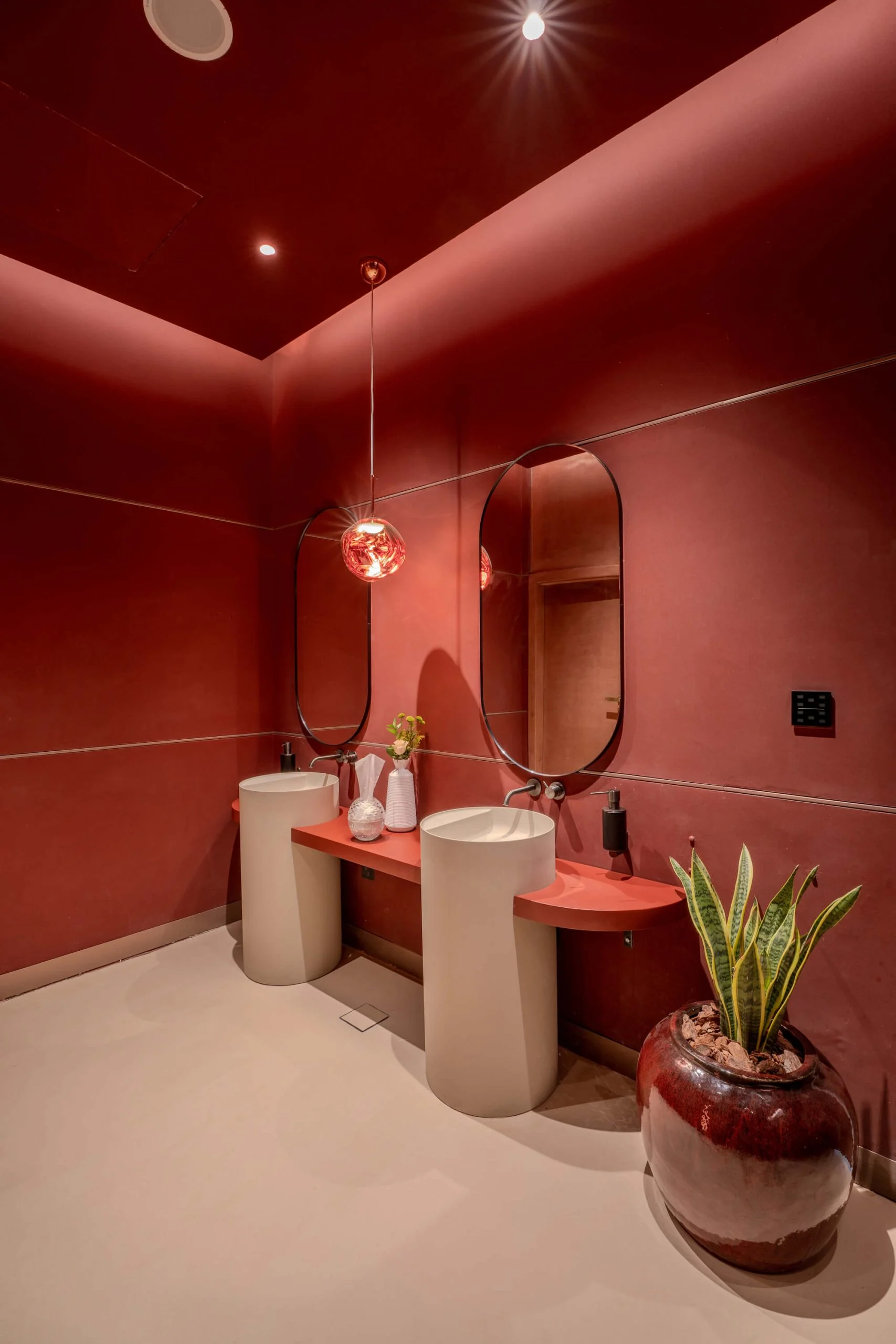 Bagno rosso con due lavabi bianchi a colonna, specchi ovali, una lampada a sospensione e una grande pianta in vaso – King Fahad Cultural Center, Riyadh, Arabia Saudita, 2024 – riqualificazione architettonica