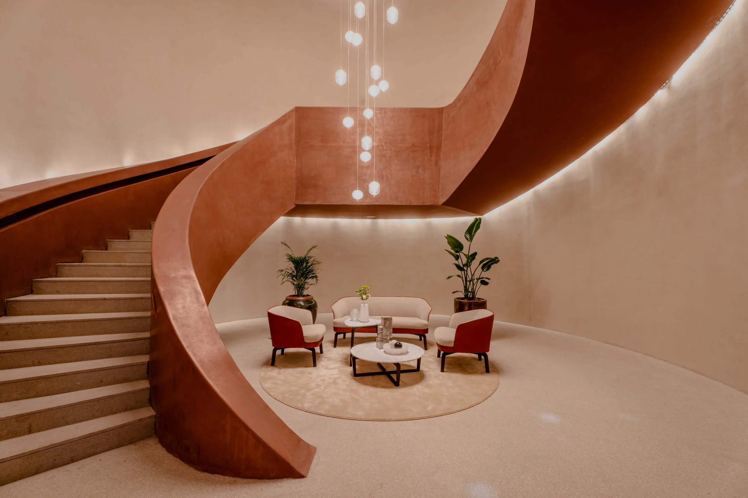 Ampia scala elicoidale in terracotta intorno a una piccola zona salotto con poltrone rosse e lampade sospese – King Fahad Cultural Center, Riyadh, Arabia Saudita, 2024 – riqualificazione architettonica