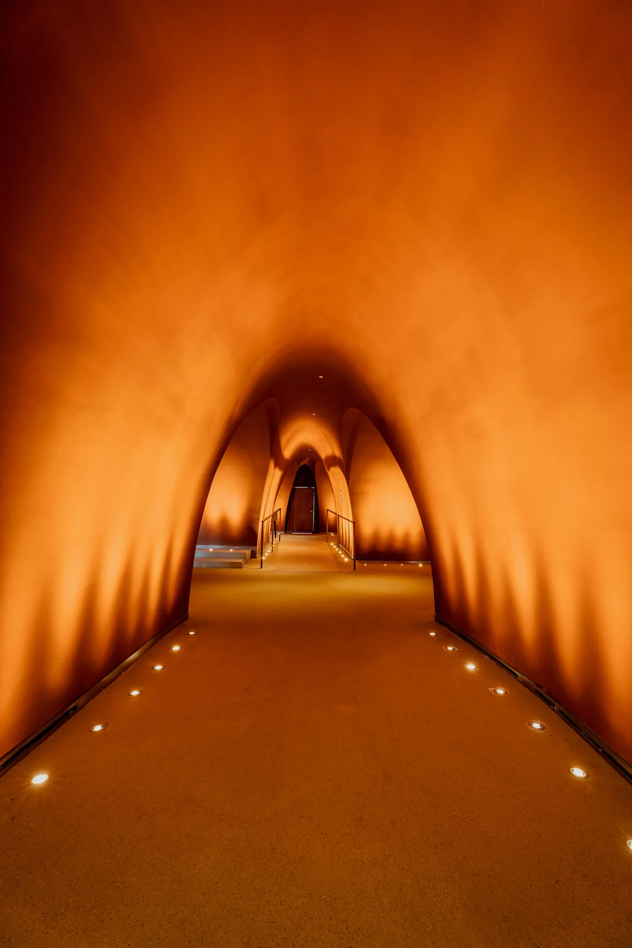 Corridoio ad arco illuminato di arancione con luci a pavimento che porta a una porta in lontananza – King Fahad Cultural Center, Riyadh, Arabia Saudita, 2024 – riqualificazione architettonica