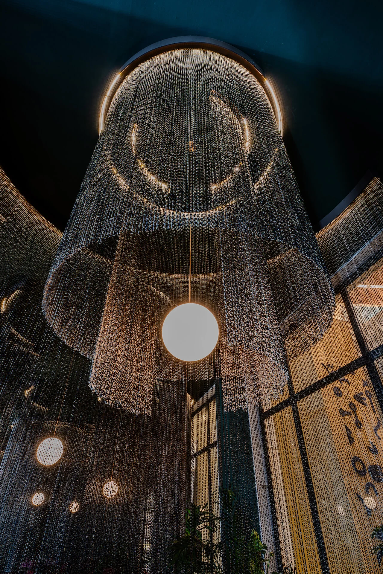 Vista dal basso di un grande lampadario a tenda di catene metalliche con una sola sfera luminosa al centro – King Fahad Cultural Center, Riyadh, Arabia Saudita, 2024 – riqualificazione architettonica