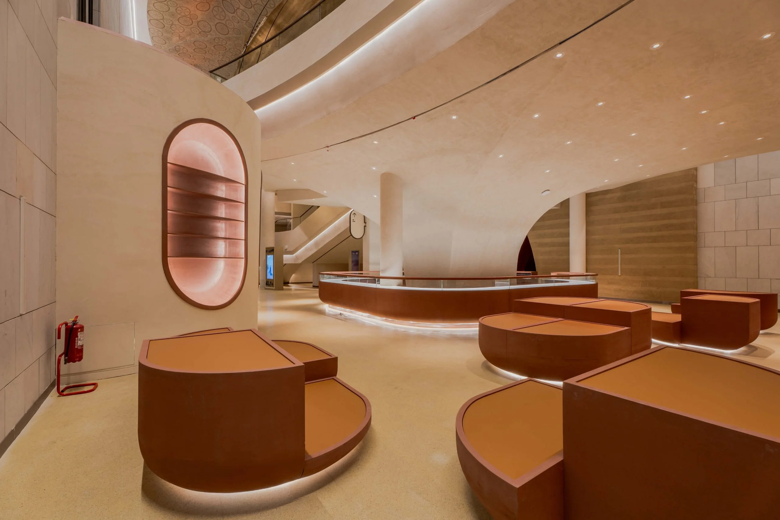 Lobby con basamenti espositivi rivestiti in pelle, un bancone curvo in vetro e nicchie ovali retroilluminate nelle pareti in pietra – King Fahad Cultural Center, Riyadh, Arabia Saudita, 2024 – riqualificazione architettonica