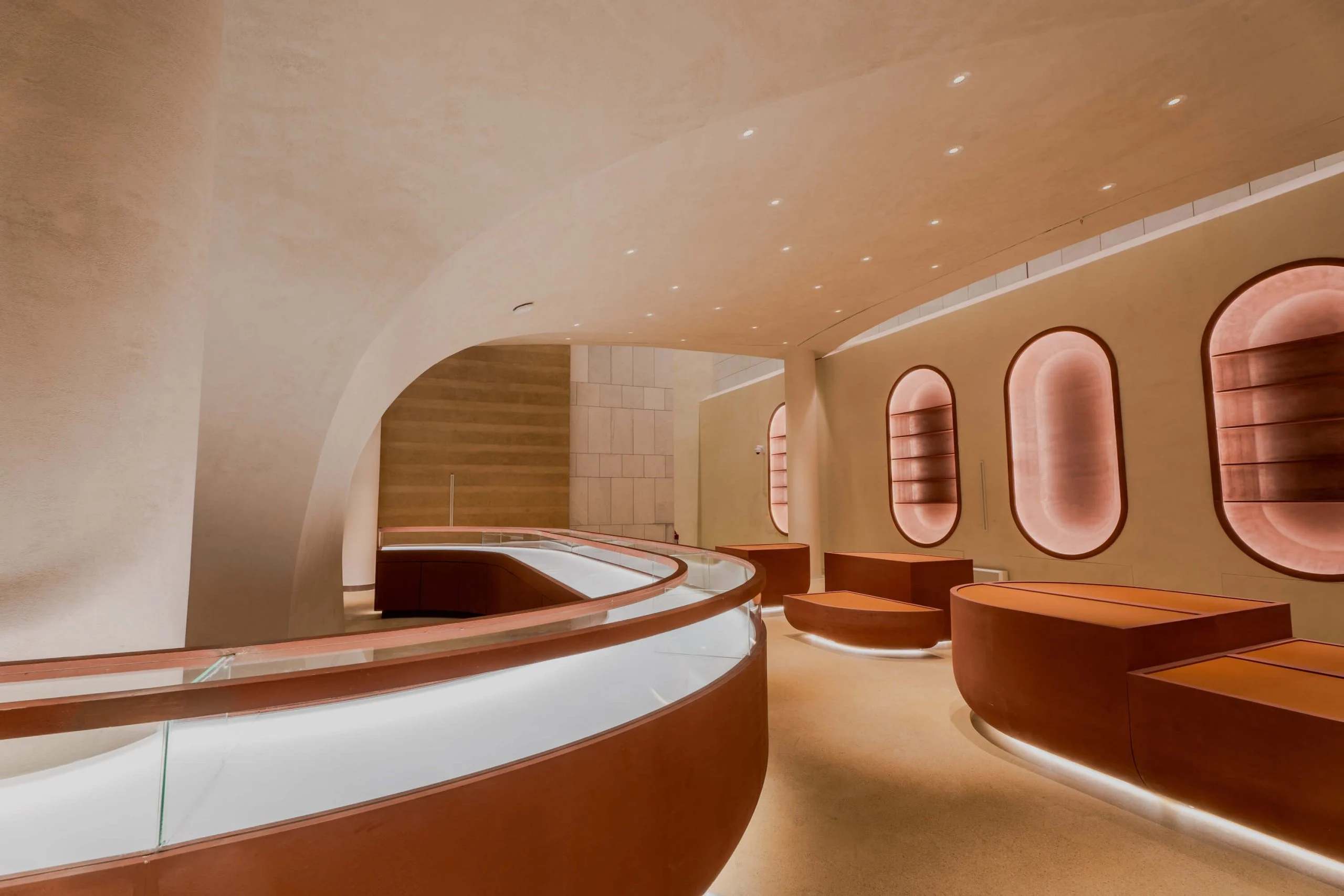 Bancone espositivo curvo in vetro e sedute rivestite in pelle accanto a una parete di nicchie ovali luminose – King Fahad Cultural Center, Riyadh, Arabia Saudita, 2024 – riqualificazione architettonica
