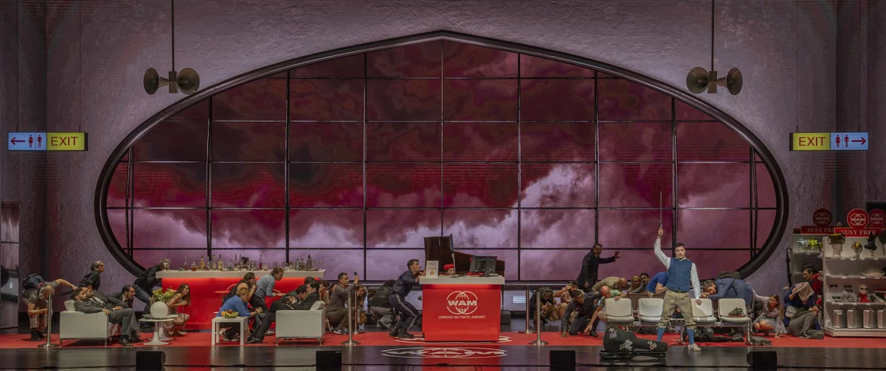 Scenografia dell'aeroporto con la finestra ovale piena di nuvole rosse, passeggeri distesi intorno al banco del check-in – Une Folle Journée Mozart Gala, Salisburgo, Austria, 2024 – scenografia d'opera