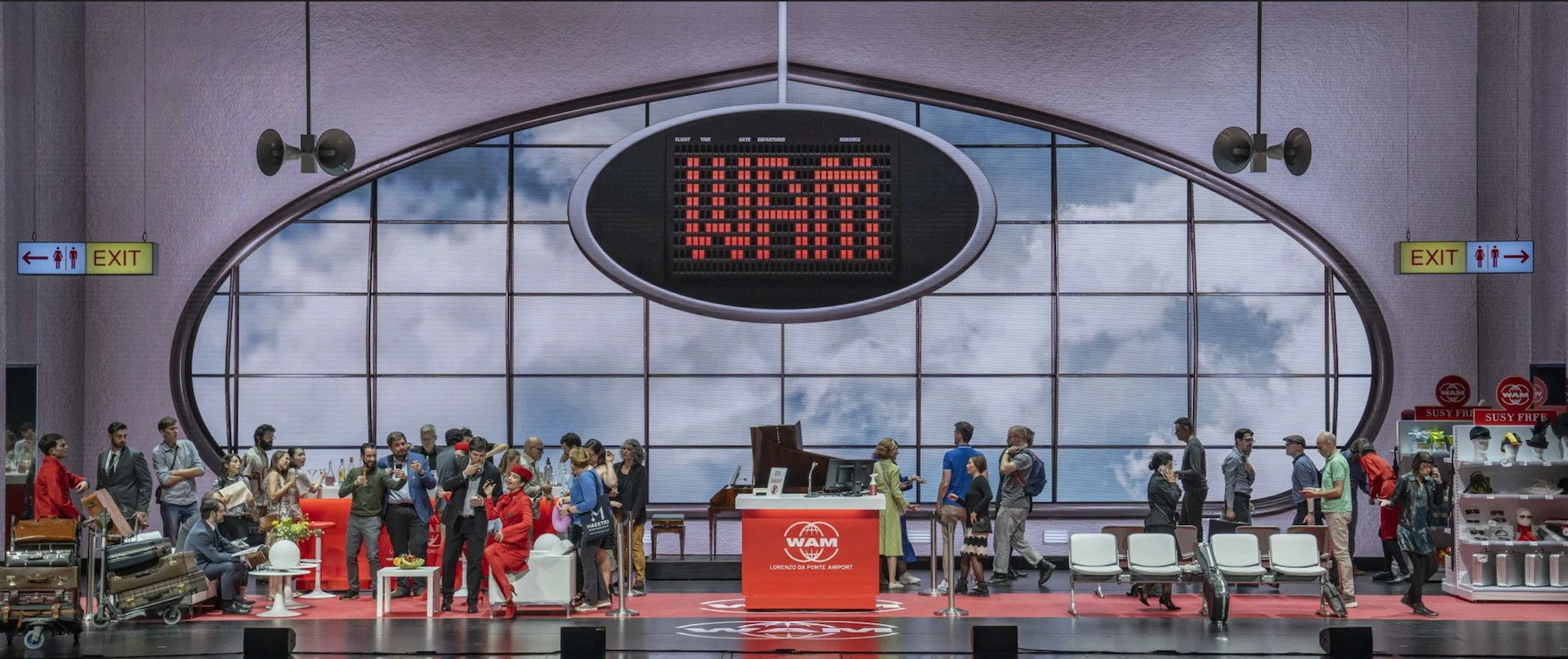 Scenografia dell'aeroporto con un tabellone voli rosso sopra la finestra ovale e passeggeri in attesa – Une Folle Journée Mozart Gala, Salisburgo, Austria, 2024 – scenografia d'opera