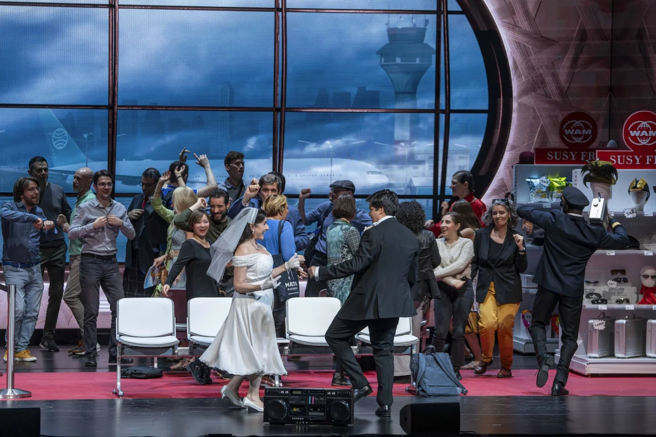 Sposi che ballano tra passeggeri in festa davanti alla finestra del terminal e alla torre di controllo – Une Folle Journée Mozart Gala, Salisburgo, Austria, 2024 – scenografia d'opera