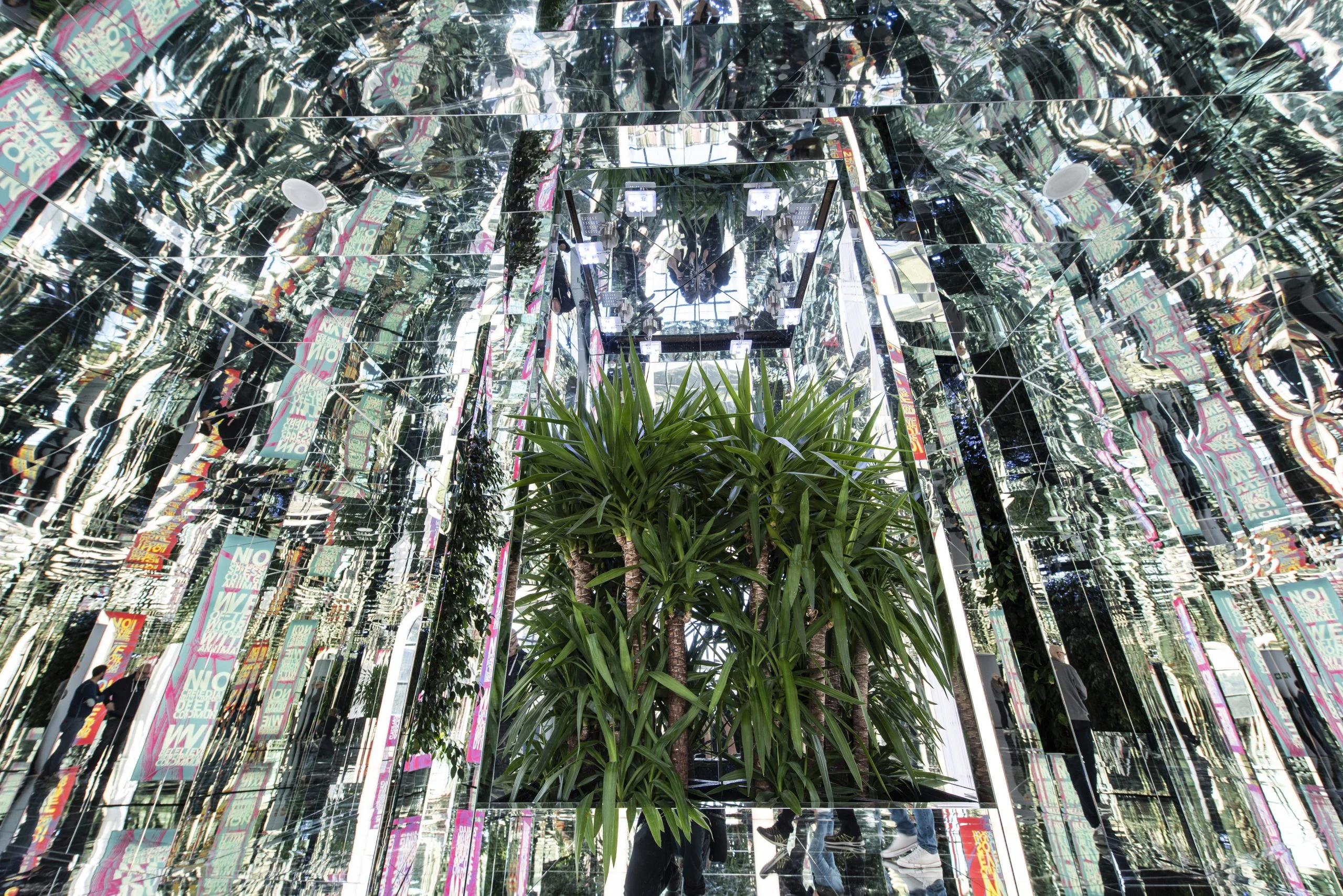 Stanza a specchi caleidoscopica con una palma in vaso al centro, moltiplicata dai riflessi su ogni lato – La Nazione delle Piante alla Triennale, Milano, Italia, 2019 – allestimento espositivo