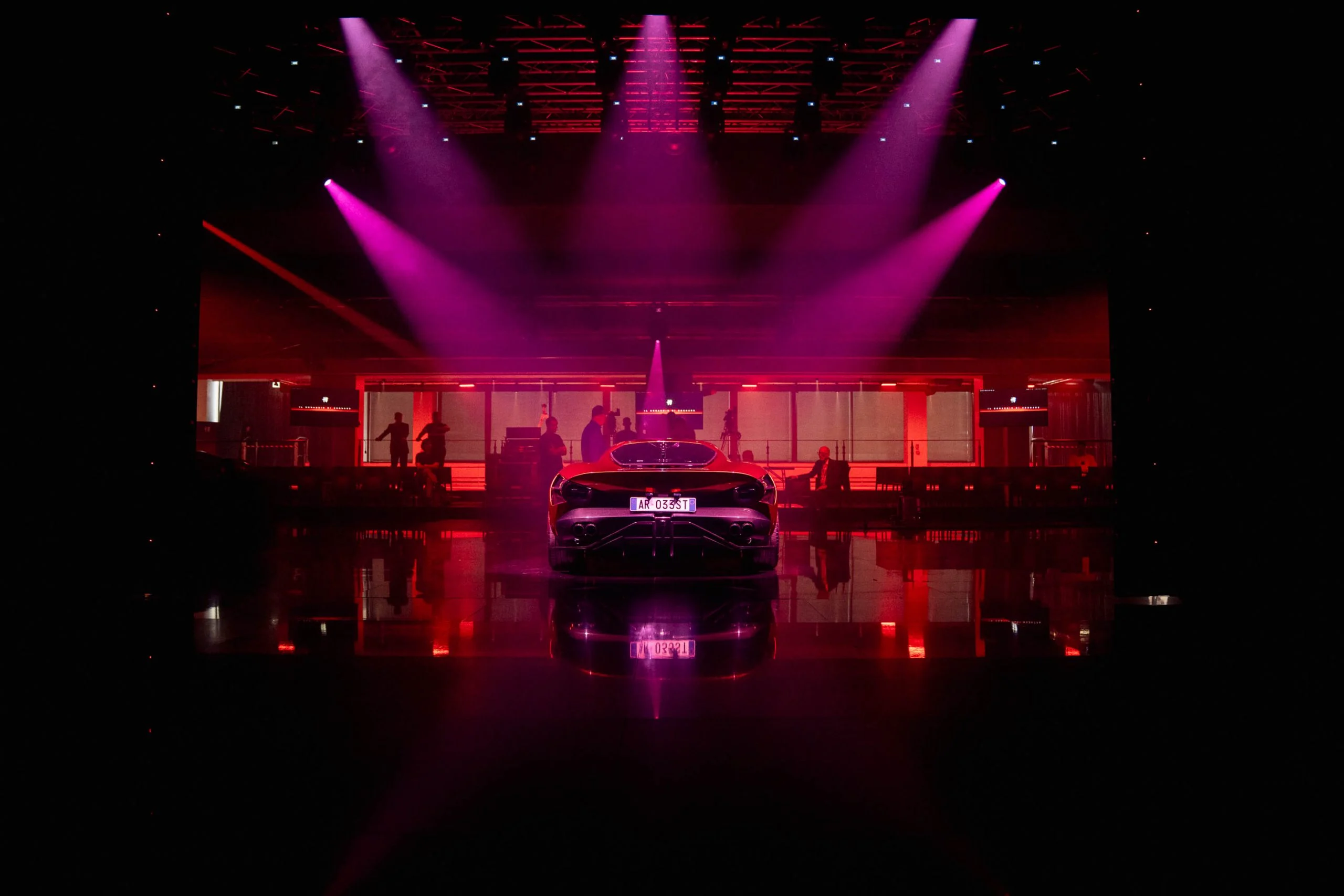 Vista posteriore della nuova auto sotto riflettori magenta, al centro di un pavimento riflettente – Presentazione Alfa Romeo 33 Stradale, Arese, Italia, 2023 – progettazione di eventi
