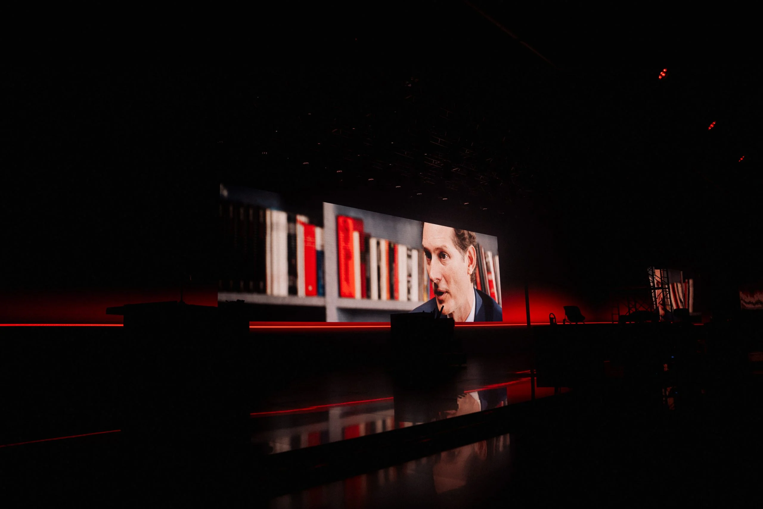 Palco buio con una lunga parete LED che mostra un relatore davanti a una libreria – Presentazione Alfa Romeo 33 Stradale, Arese, Italia, 2023 – progettazione di eventi