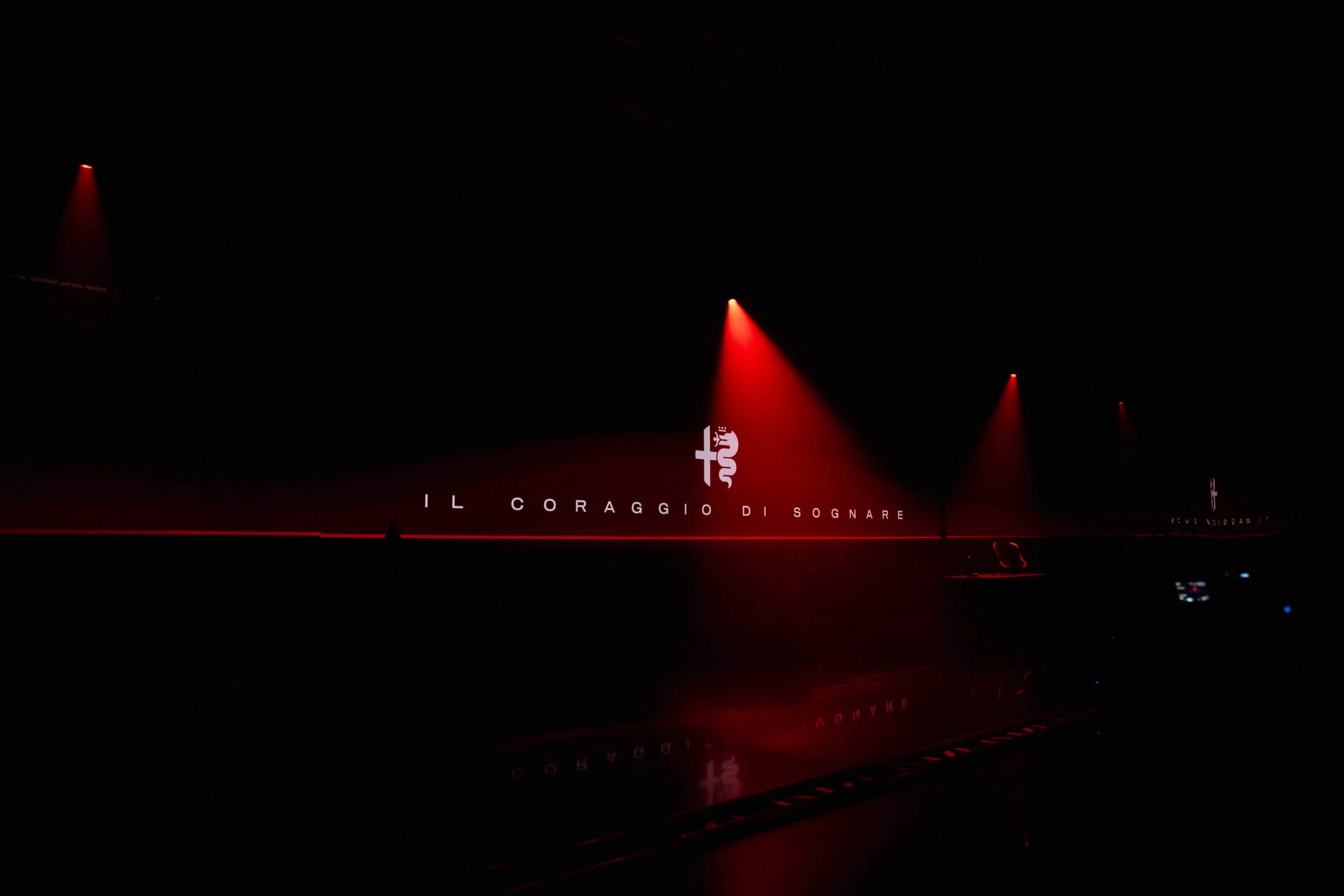 Logo Alfa Romeo e la scritta Il Coraggio di Sognare su una parete scura sotto riflettori rossi – Presentazione Alfa Romeo 33 Stradale, Arese, Italia, 2023 – progettazione di eventi