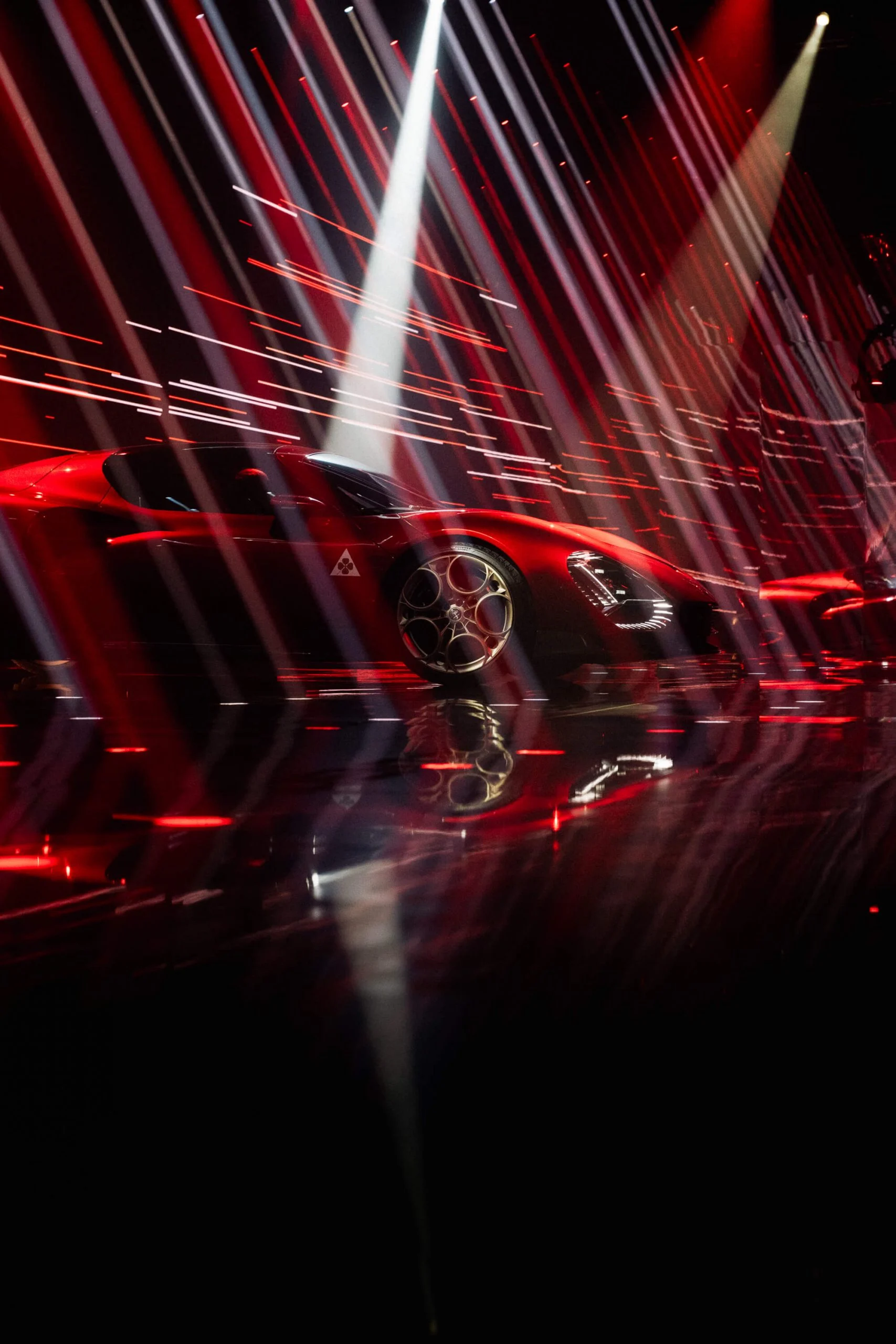 Fiancata dell'auto rossa attraversata da strisce di luce bianca e rossa, riflessa in un pavimento lucido – Presentazione Alfa Romeo 33 Stradale, Arese, Italia, 2023 – progettazione di eventi