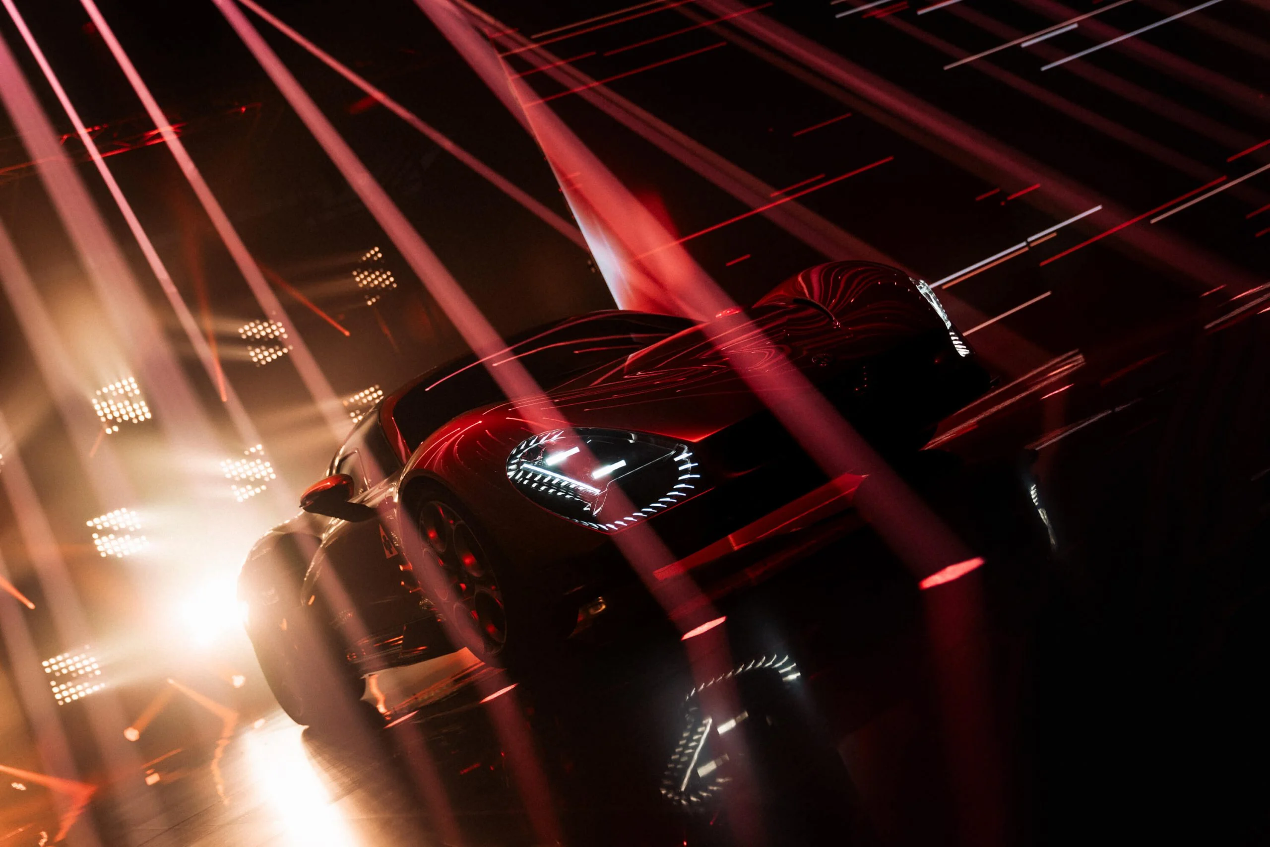 Vista frontale dal basso dell'auto sotto fasci di luce rossa incrociati e intense luci di scena bianche – Presentazione Alfa Romeo 33 Stradale, Arese, Italia, 2023 – progettazione di eventi