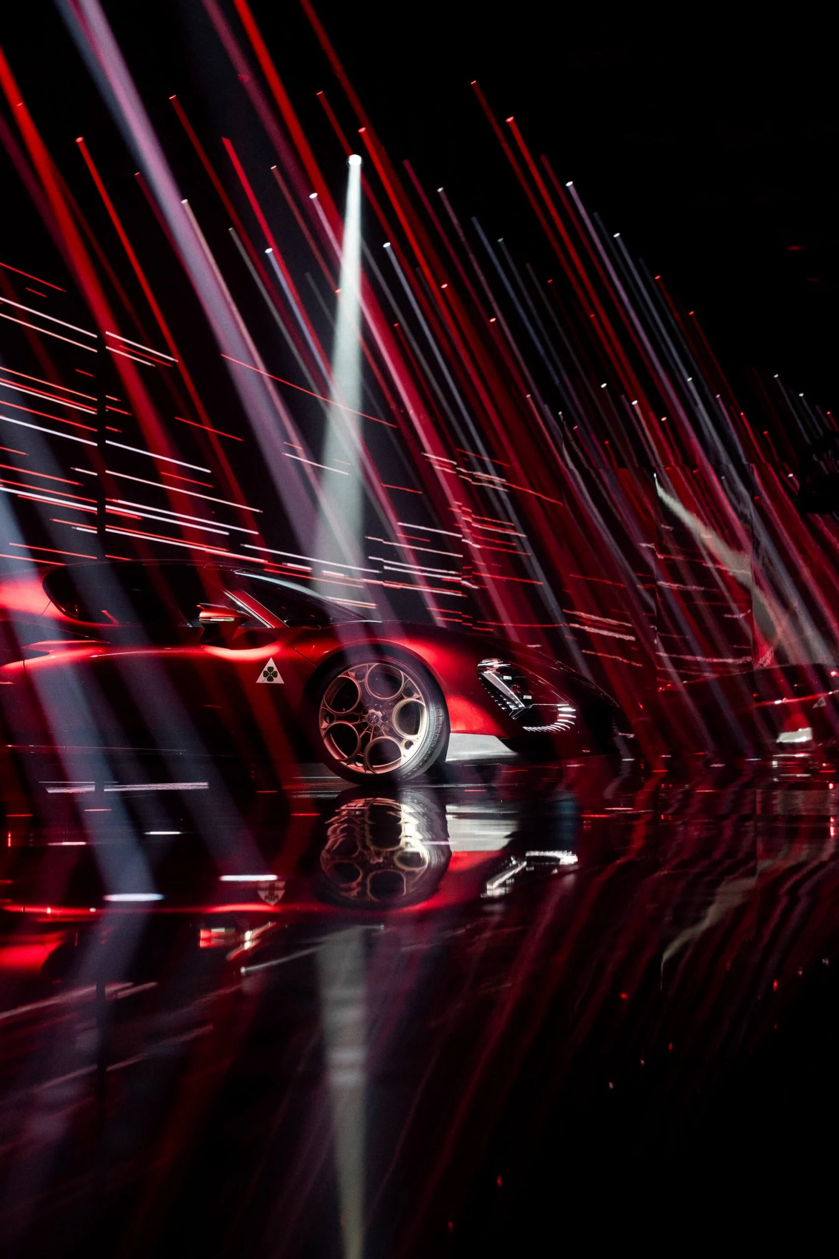 33 Stradale rossa di profilo dietro una fitta cortina di strisce di luce rossa e bianca – Presentazione Alfa Romeo 33 Stradale, Arese, Italia, 2023 – progettazione di eventi