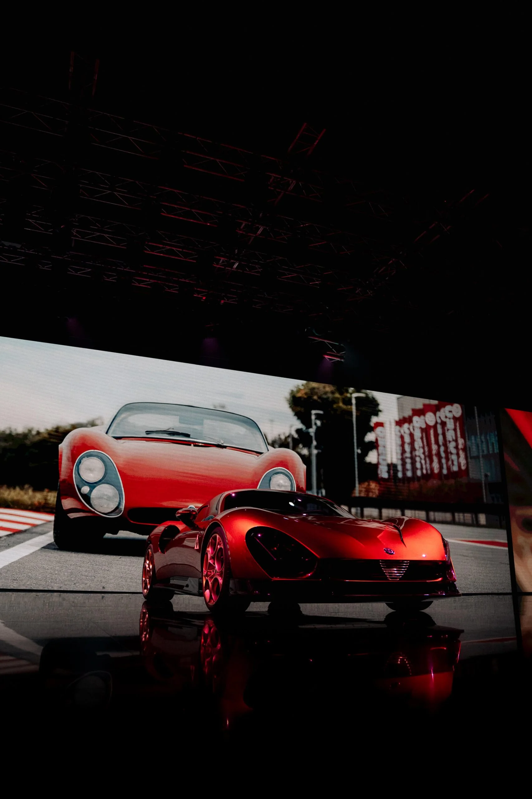 Nuova 33 Stradale sul palco davanti a uno schermo gigante con l'auto originale degli anni Sessanta in pista – Presentazione Alfa Romeo 33 Stradale, Arese, Italia, 2023 – progettazione di eventi