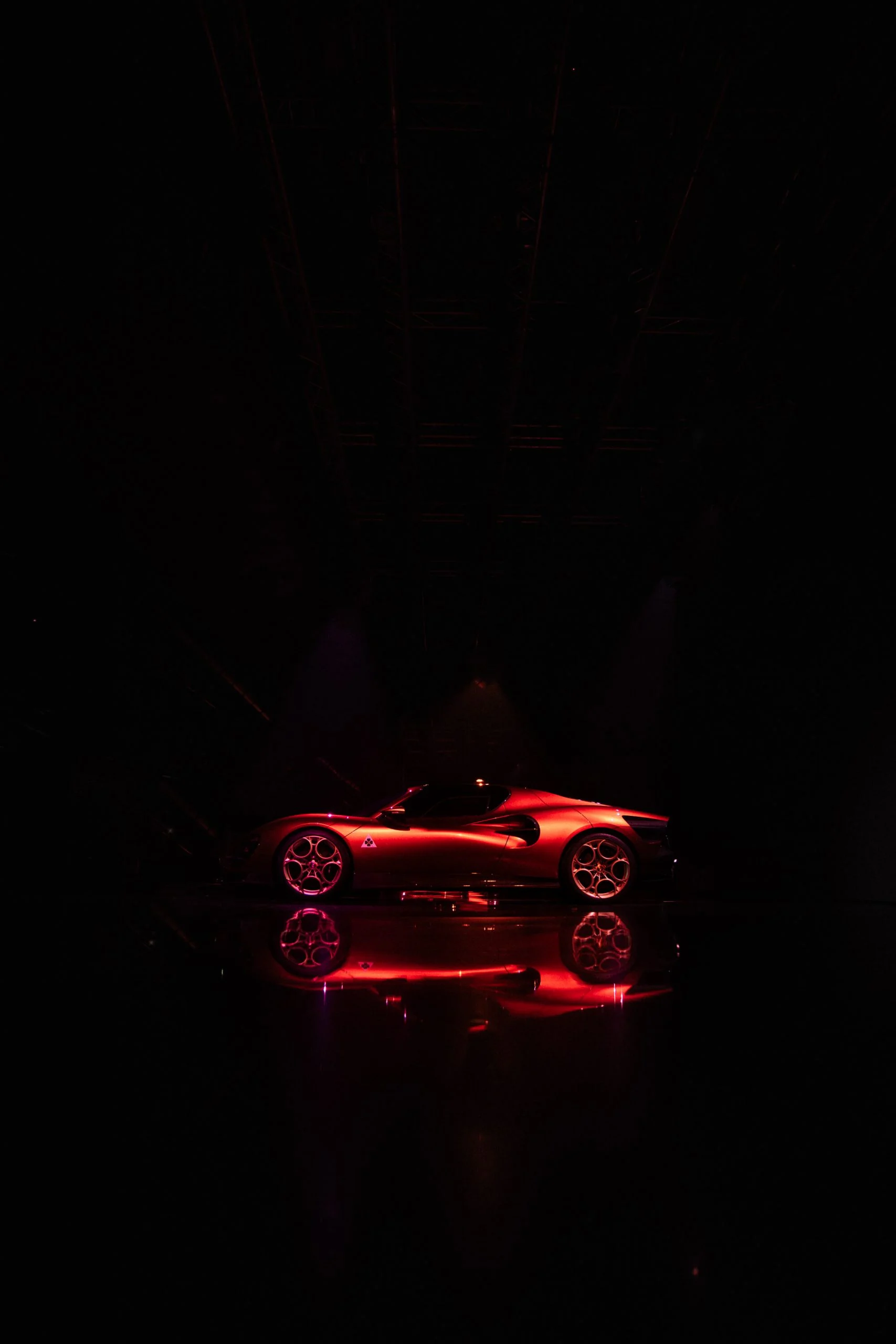 33 Stradale rossa di profilo, sola in uno spazio buio e riflessa sul pavimento – Presentazione Alfa Romeo 33 Stradale, Arese, Italia, 2023 – progettazione di eventi