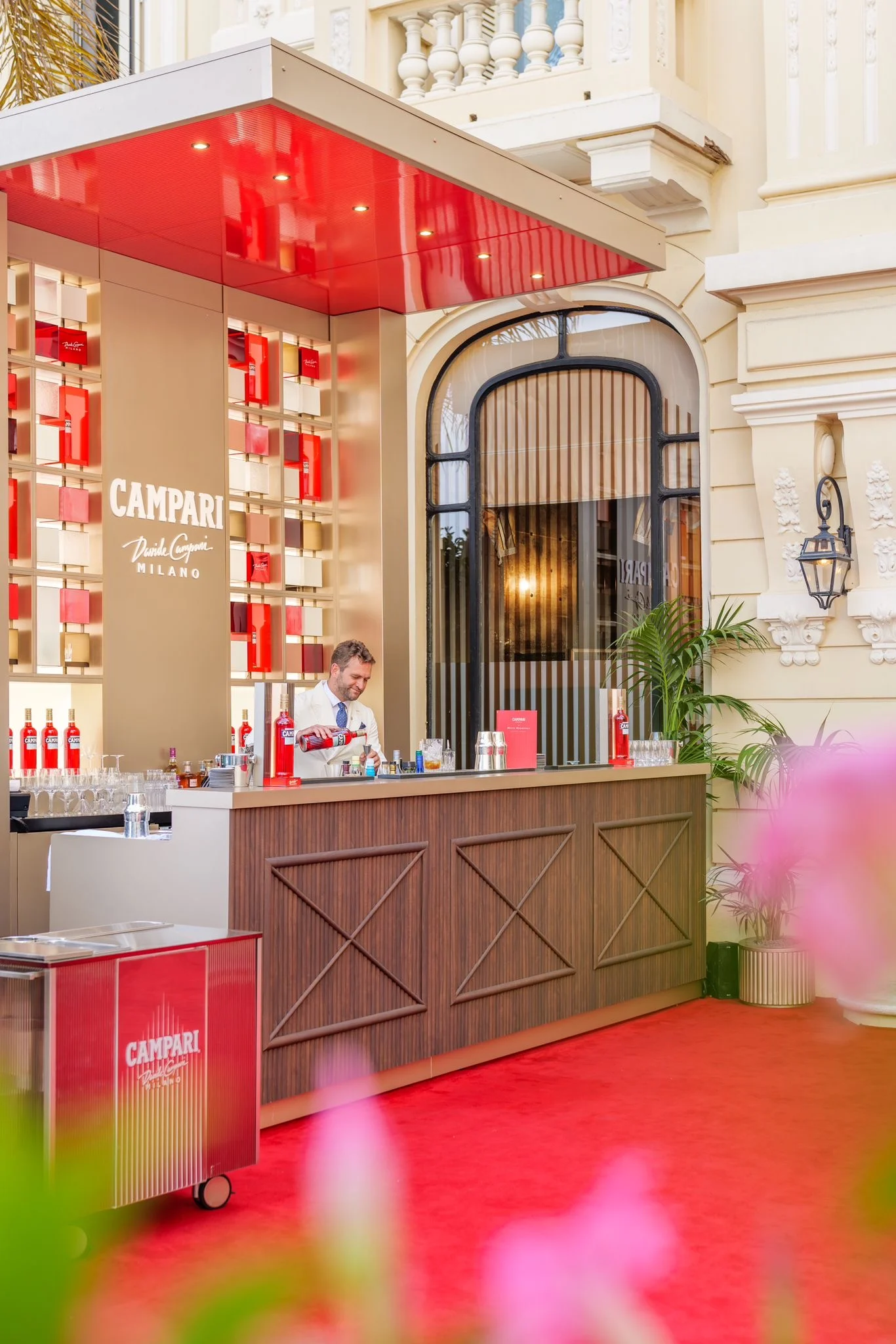 Vista laterale del bar Campari e di un carrello rosso sul tappeto rosso, con la finestra ad arco dell'hotel – Campari Pop-Up Bar all'Hôtel Hermitage, Monte Carlo, Principato di Monaco, 2024 – hospitality design
