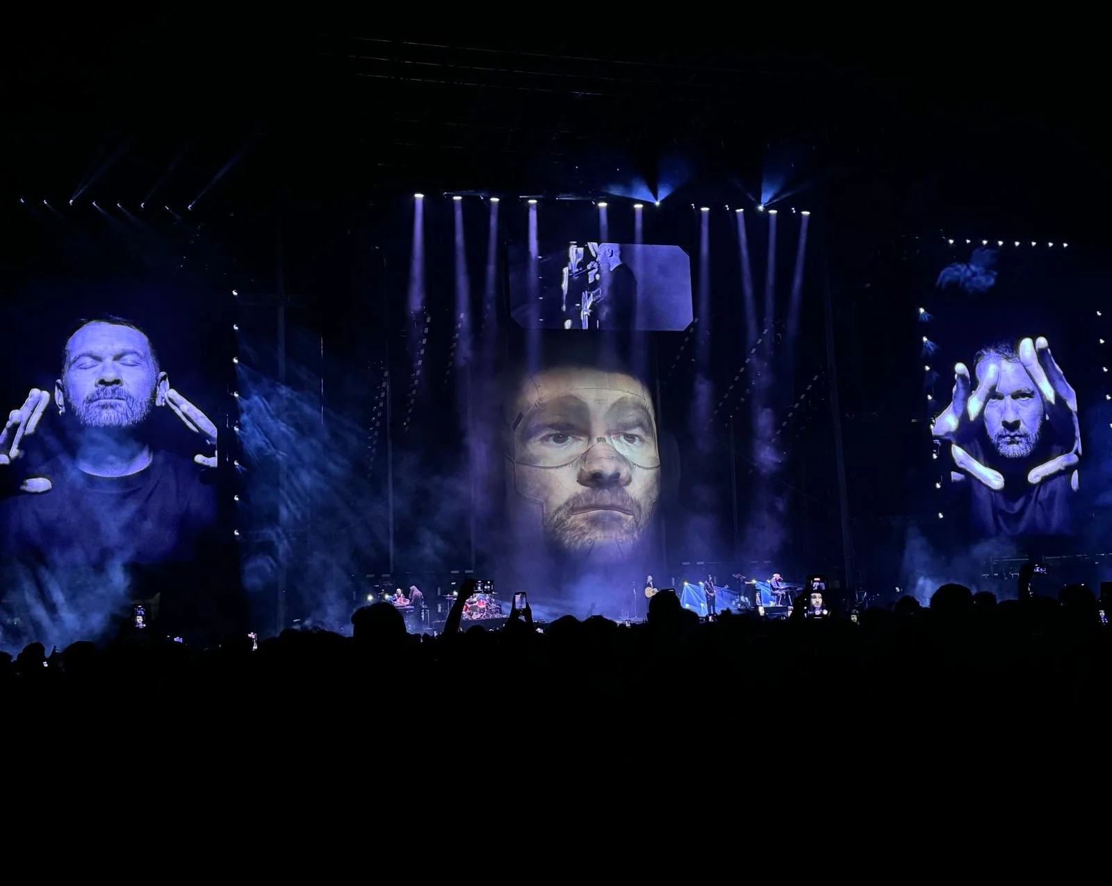Palco in luce blu con un volto proiettato sulla testa gigante e primi piani sugli schermi laterali – Negramaro Stadi 2024, Italia – scenografia per concerti