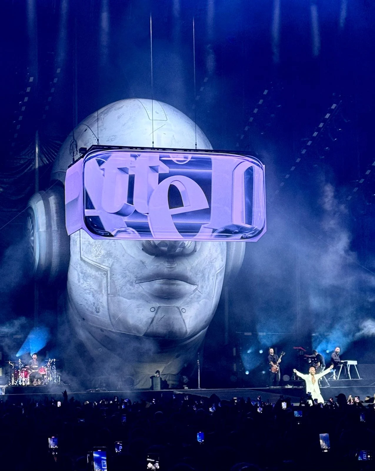 Testa gigante in luce blu, la visiera LED con scritte grafiche sopra la band e il cantante – Negramaro Stadi 2024, Italia – scenografia per concerti
