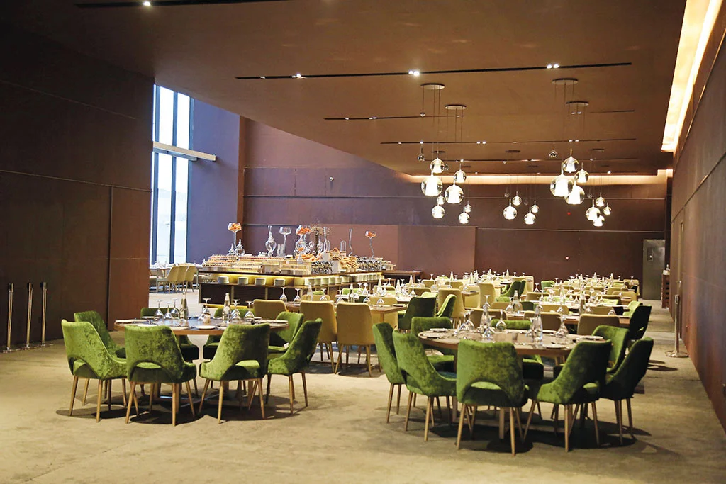 Sala banchetti con sedie in velluto verde, tavoli rotondi apparecchiati e lampade a sospensione in vetro – Maraya Concert Hall, AlUla, Arabia Saudita, 2019 – architettura