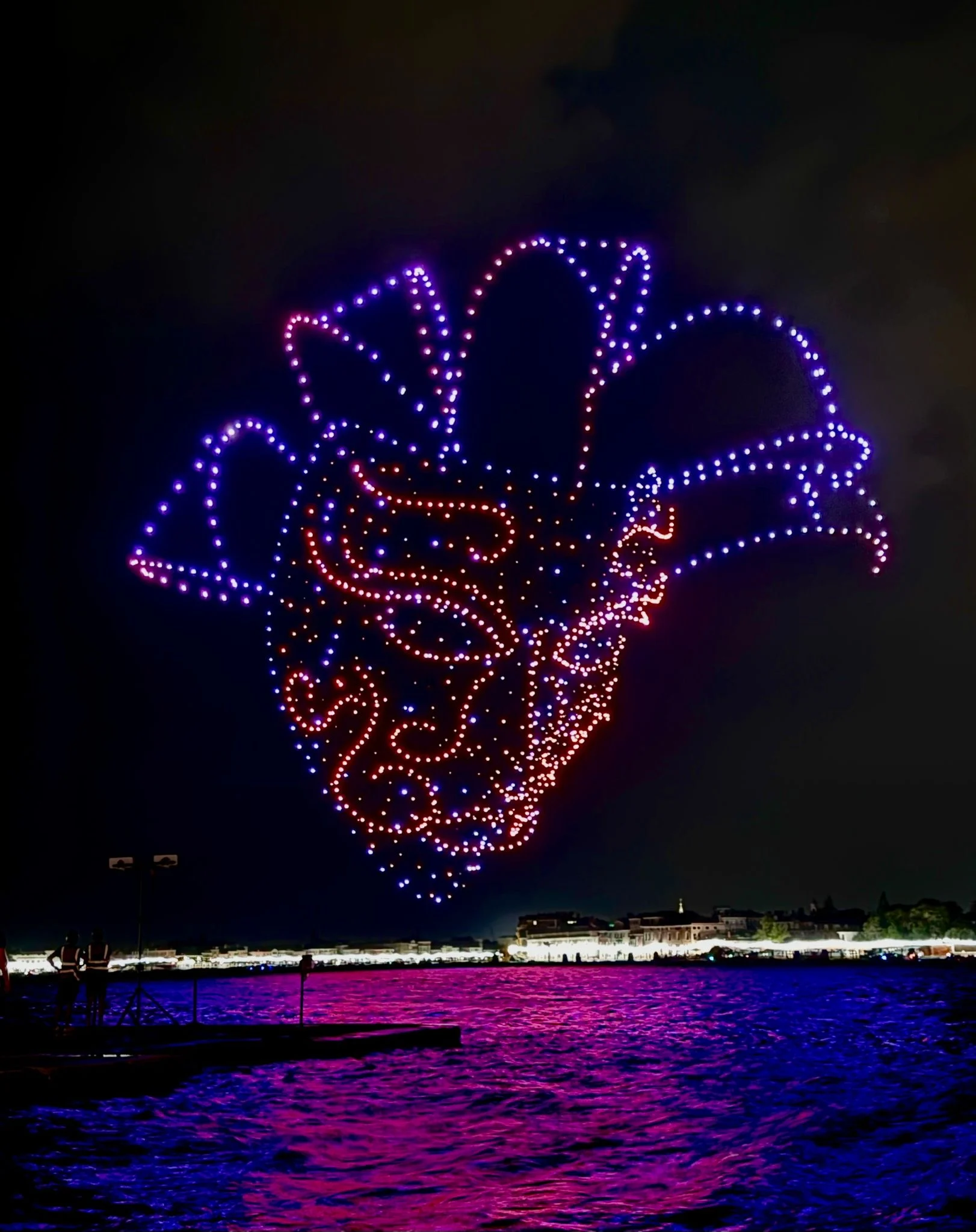 Formazione di droni a forma di maschera del Carnevale di Venezia con luci viola e arancioni sopra la laguna – Aperol Redentore Drone Show, Venezia, Italia, 2024 – direzione creativa