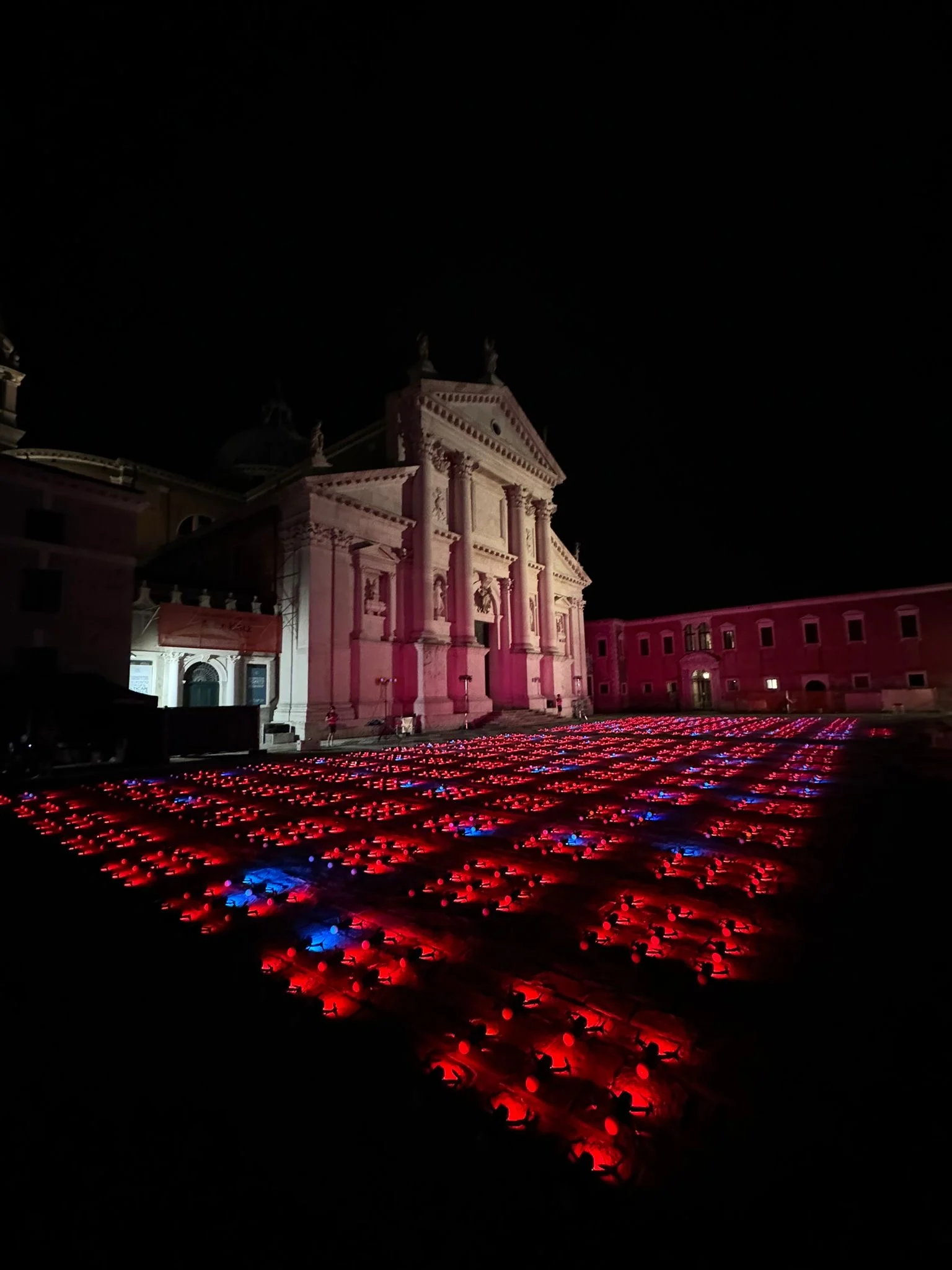 File di droni accesi di rosso e blu a terra davanti alla facciata illuminata di una chiesa di notte – Aperol Redentore Drone Show, Venezia, Italia, 2024 – direzione creativa