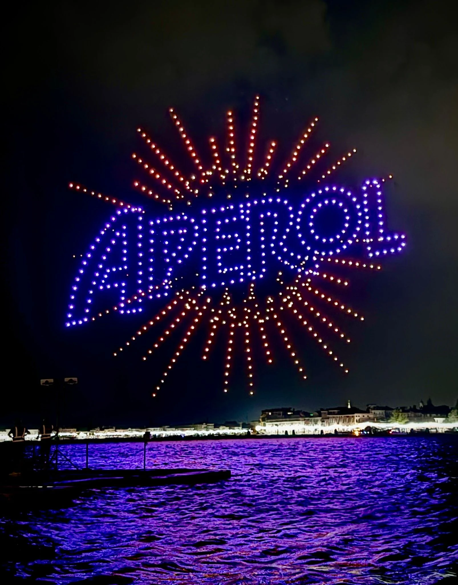 Droni che compongono la scritta Aperol in blu con raggi arancioni sopra la laguna di notte – Aperol Redentore Drone Show, Venezia, Italia, 2024 – direzione creativa