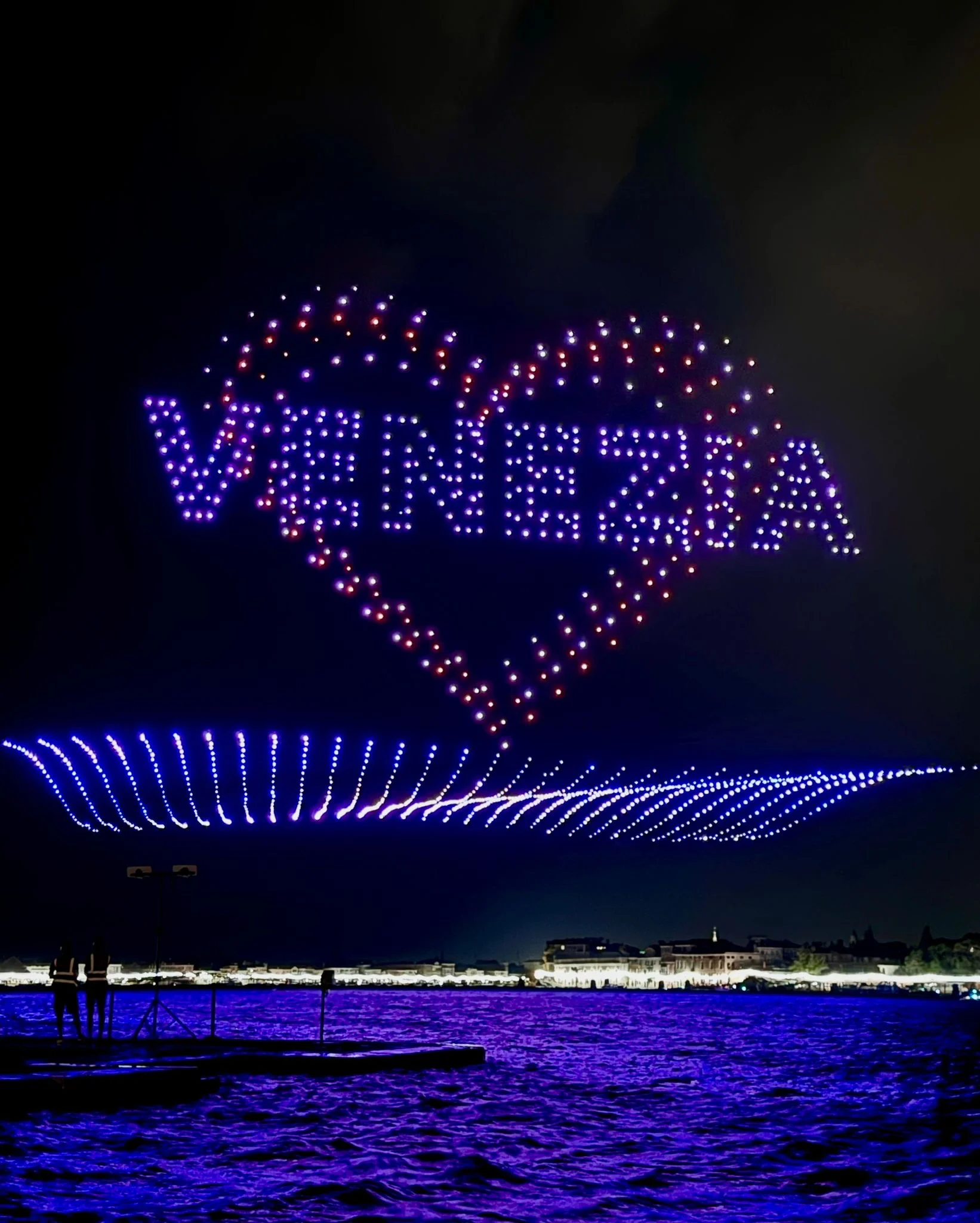 Droni che compongono la scritta Venezia dentro un cuore, sopra un'onda di luci blu sulla laguna – Aperol Redentore Drone Show, Venezia, Italia, 2024 – direzione creativa