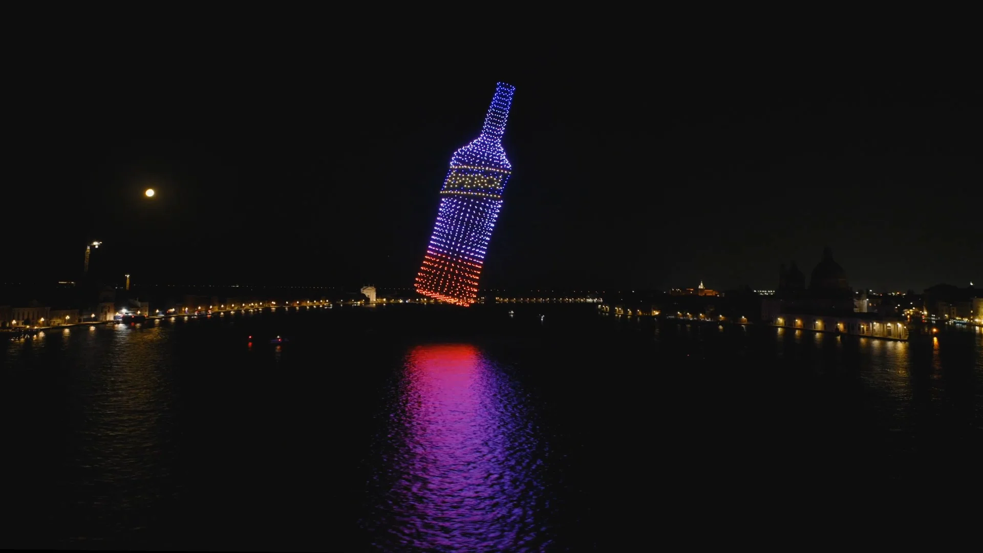 Vista aerea notturna di droni che formano una gigantesca bottiglia di Aperol sul Bacino di San Marco, riflessa nell'acqua – Aperol Redentore Drone Show, Venezia, Italia, 2024 – direzione creativa