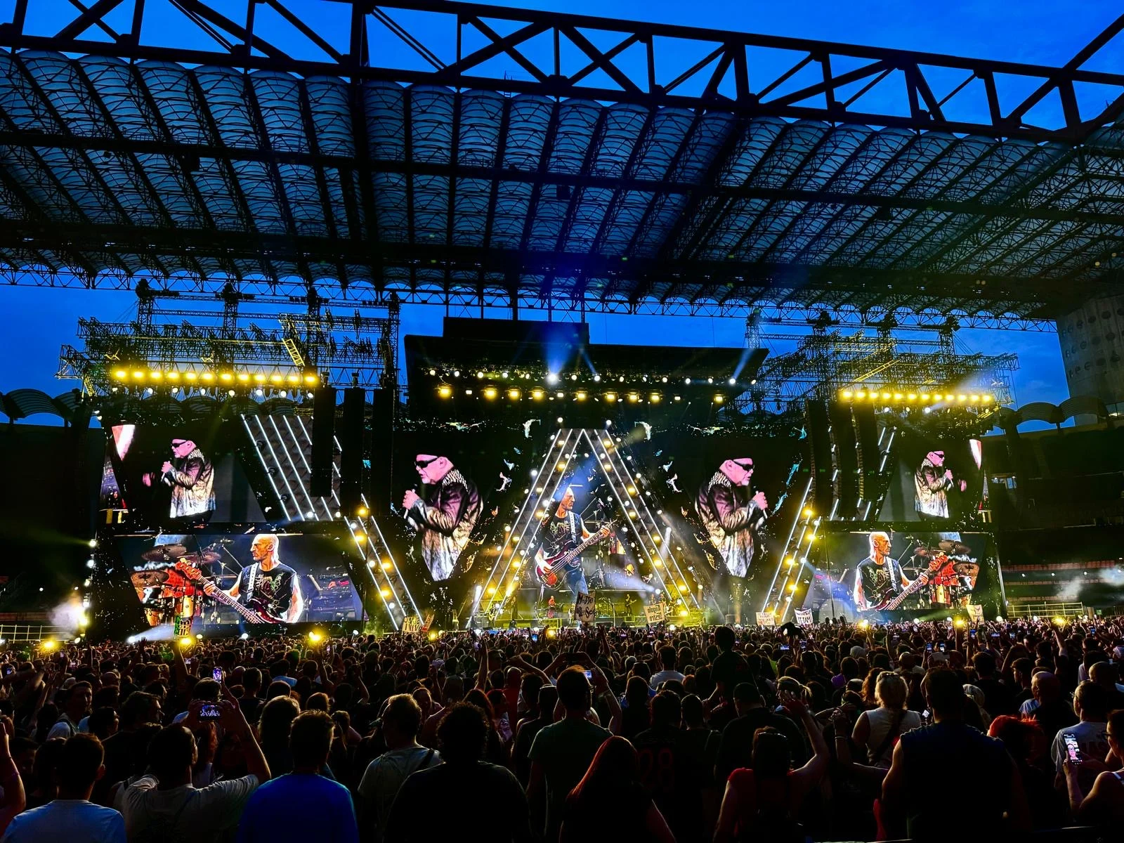 Palco di Vasco Live 2024 al tramonto sotto la copertura dello stadio, schermi LED triangolari con la band sopra la folla – Vasco Rossi Live 2024, Italia – scenografia per concerti